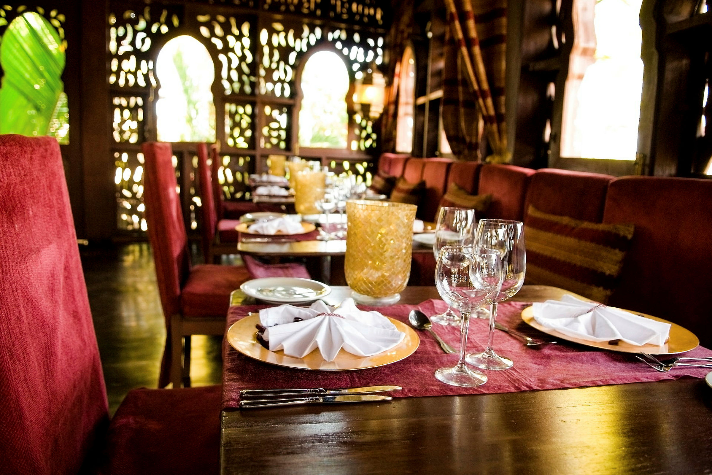 Et bord i en elegant restaurant med rødt interiør, dækket med tallerkener, glas og bestik. (AI-genereret tekst)