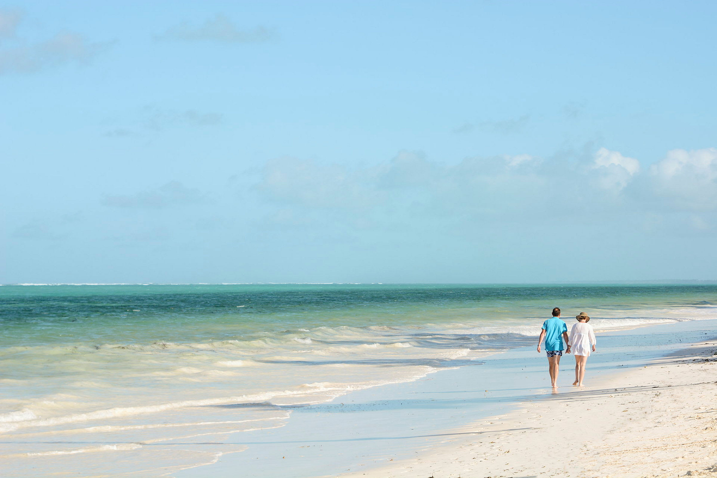 To personer går langs en sandstrand ved havet under en klar blå himmel. (AI-genereret tekst)
