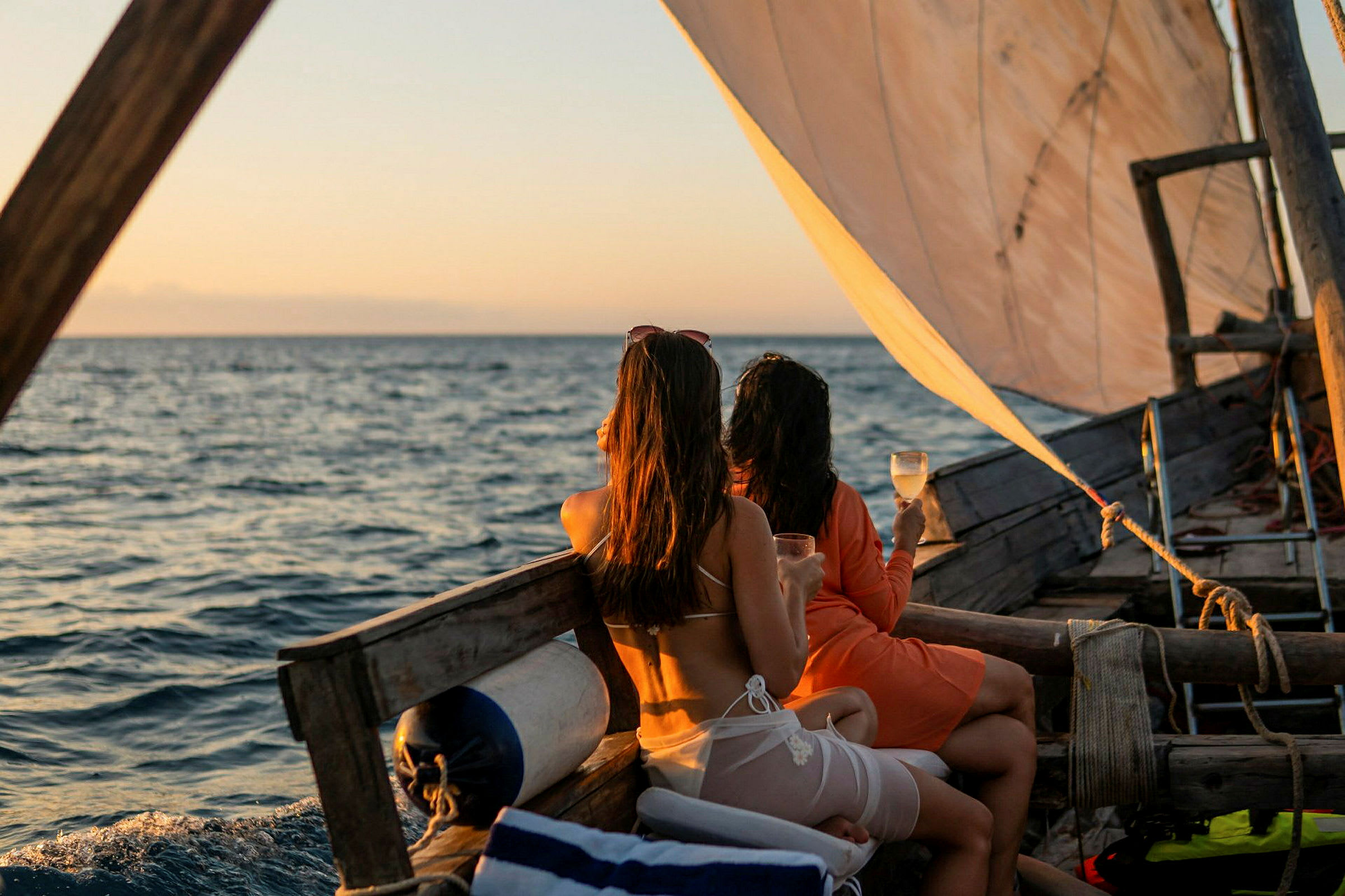To personer sidder på en sejlbåd med drikkevarer i hænderne og kigger ud over havet. (AI-genereret tekst)