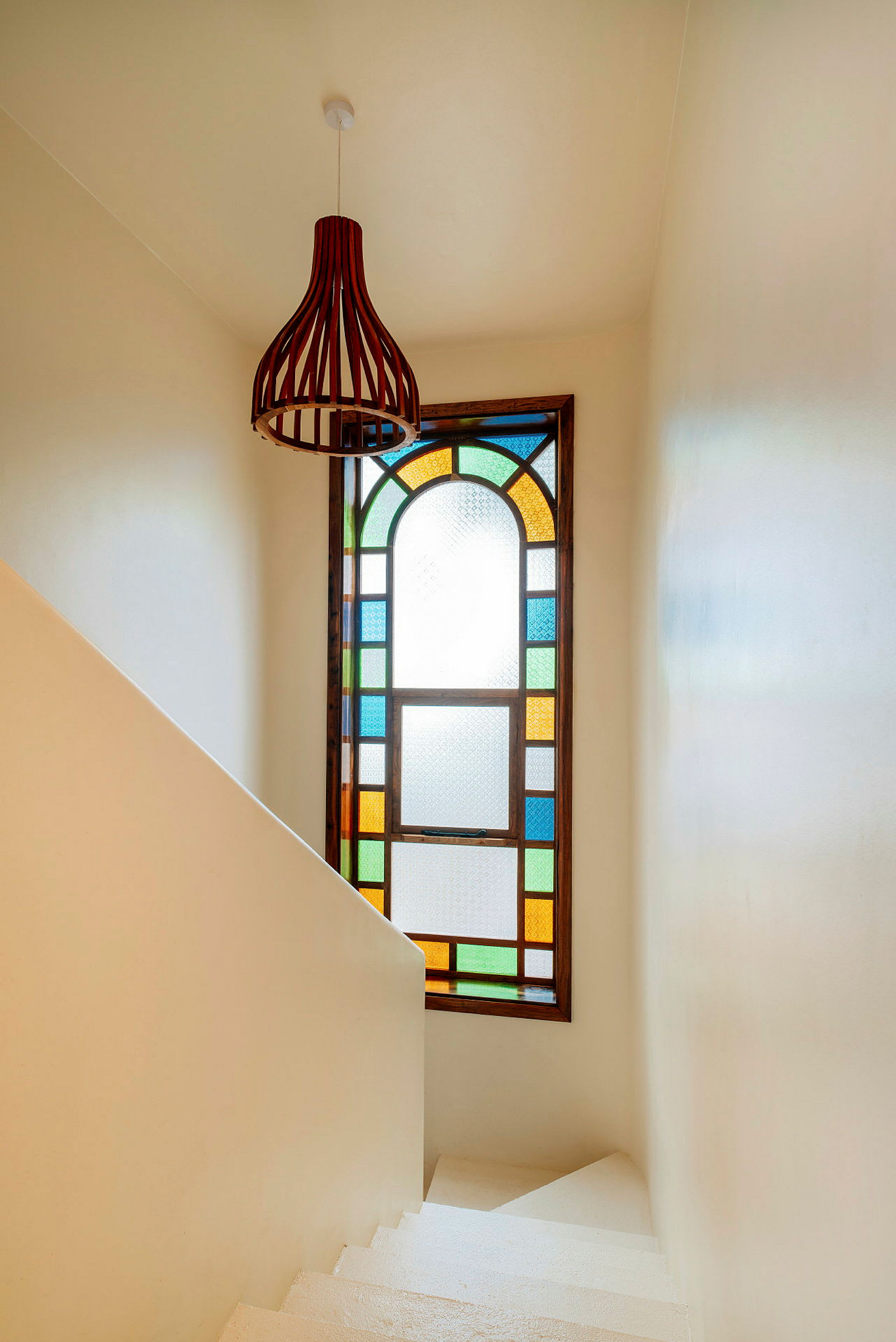 Et vindue med farvet glas og en moderne lysarmatur på væggen i en hvid trappe. (AI-genereret tekst)