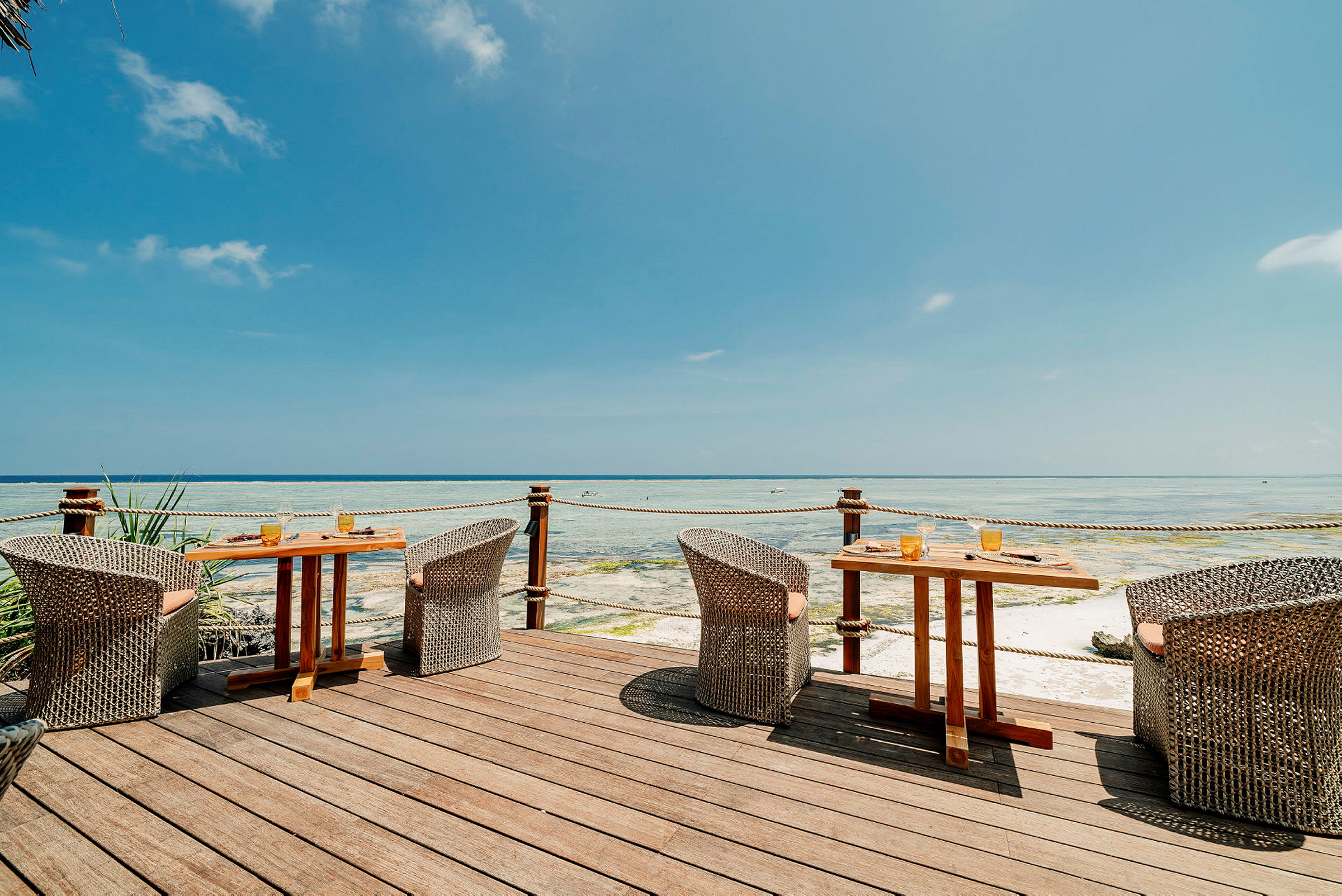 Terrasse med borde og stole med udsigt over havet, under en blå himmel. (AI-genereret tekst)