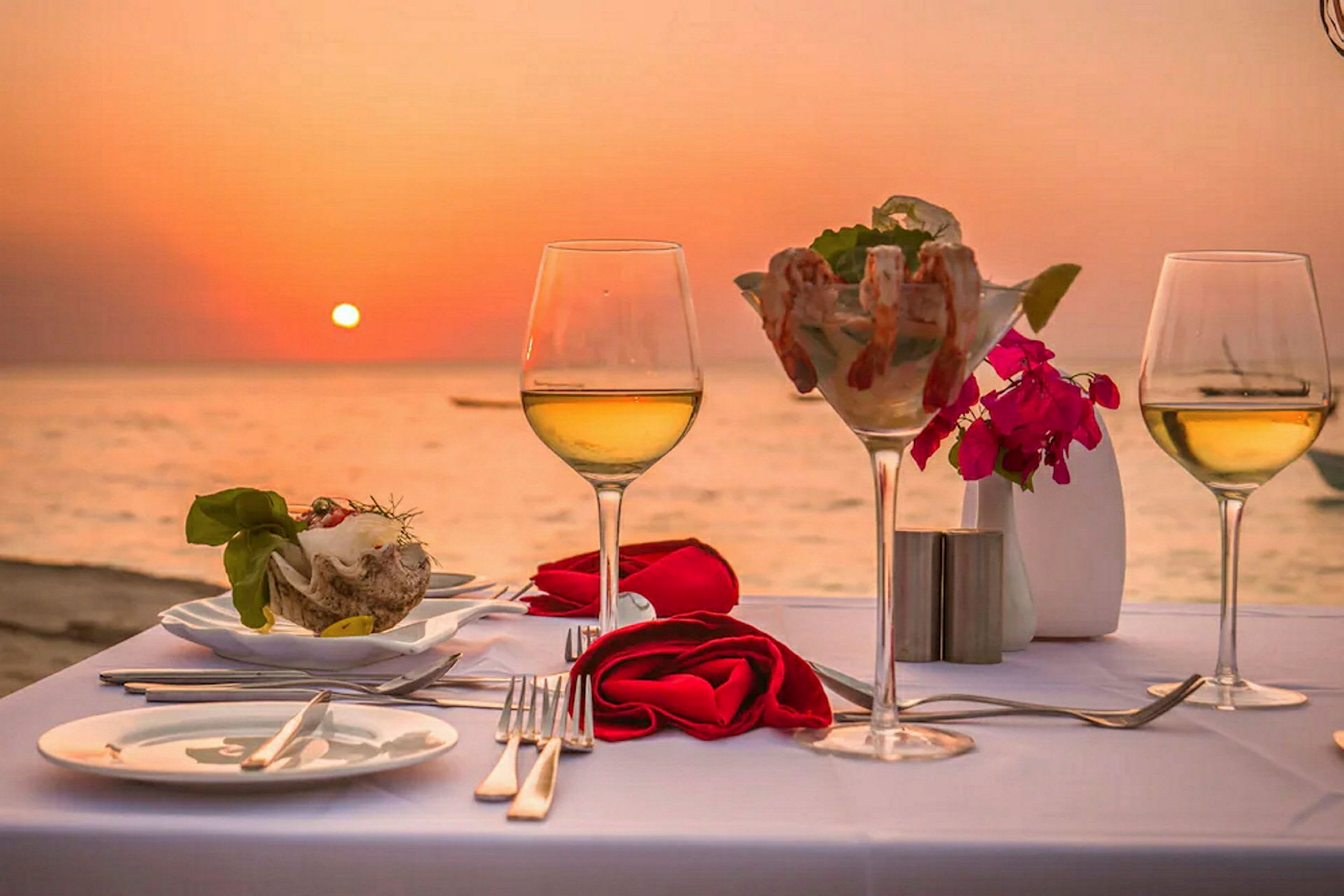 Dækket bord med vin og skaldyr med solnedgang over havet i baggrunden. (AI-genereret tekst)