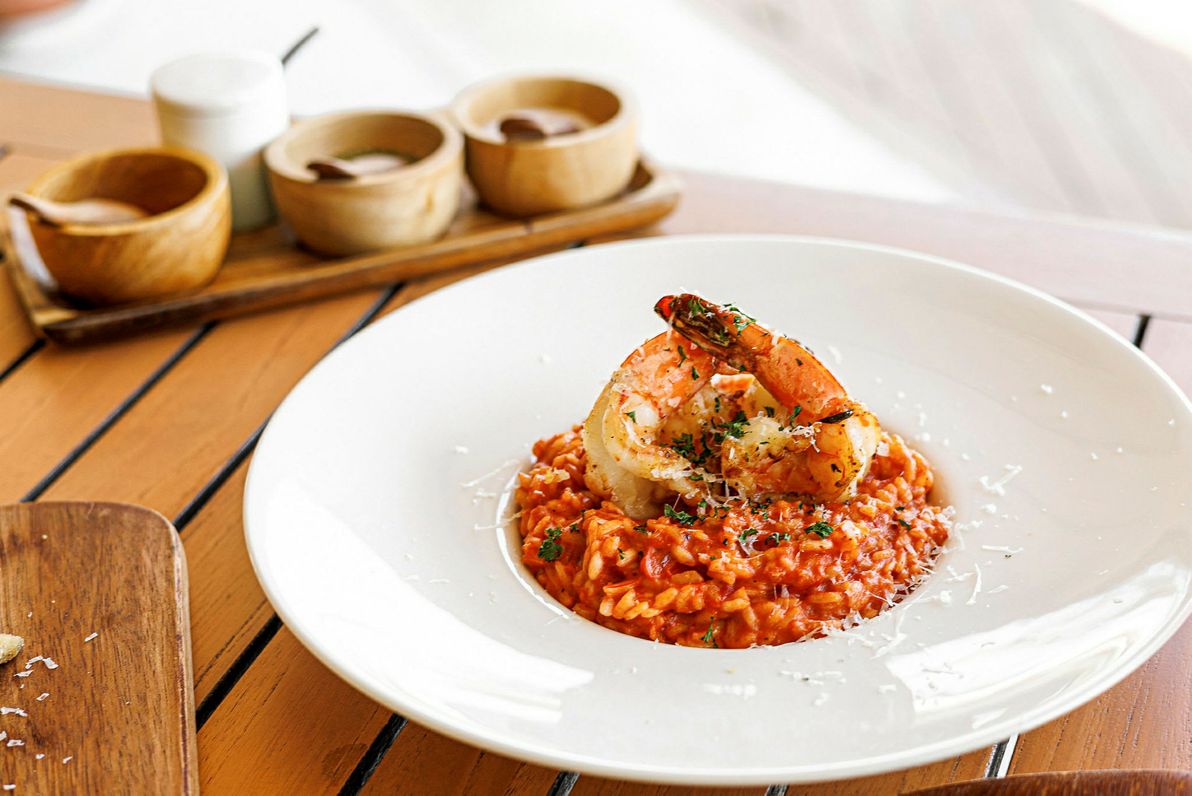 En tallerken med risotto toppet med store rejer på et bord. (AI-genereret tekst)