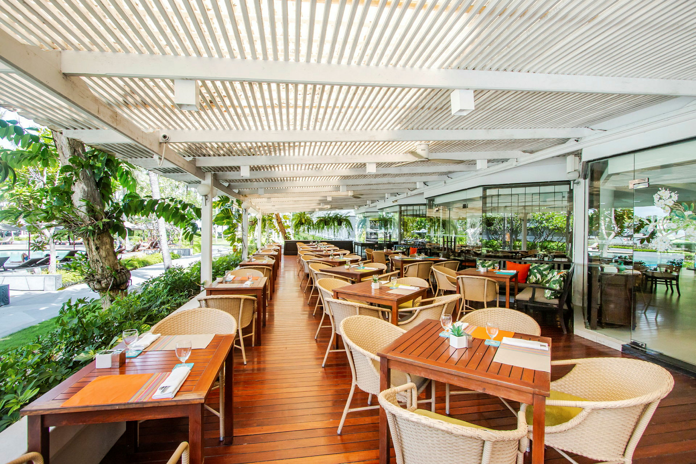Udendørsrestaurant med træborde og stole under en overdækket pergola. (AI-genereret tekst)
