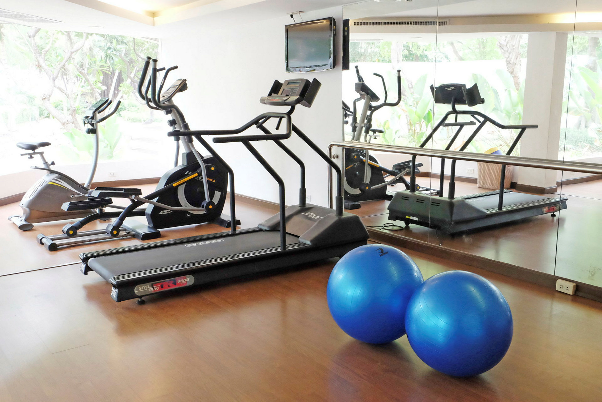 Et fitnessrum med træningsmaskiner, herunder løbebånd og motionscykel, samt to blå pilatesbolde. (AI-genereret tekst)