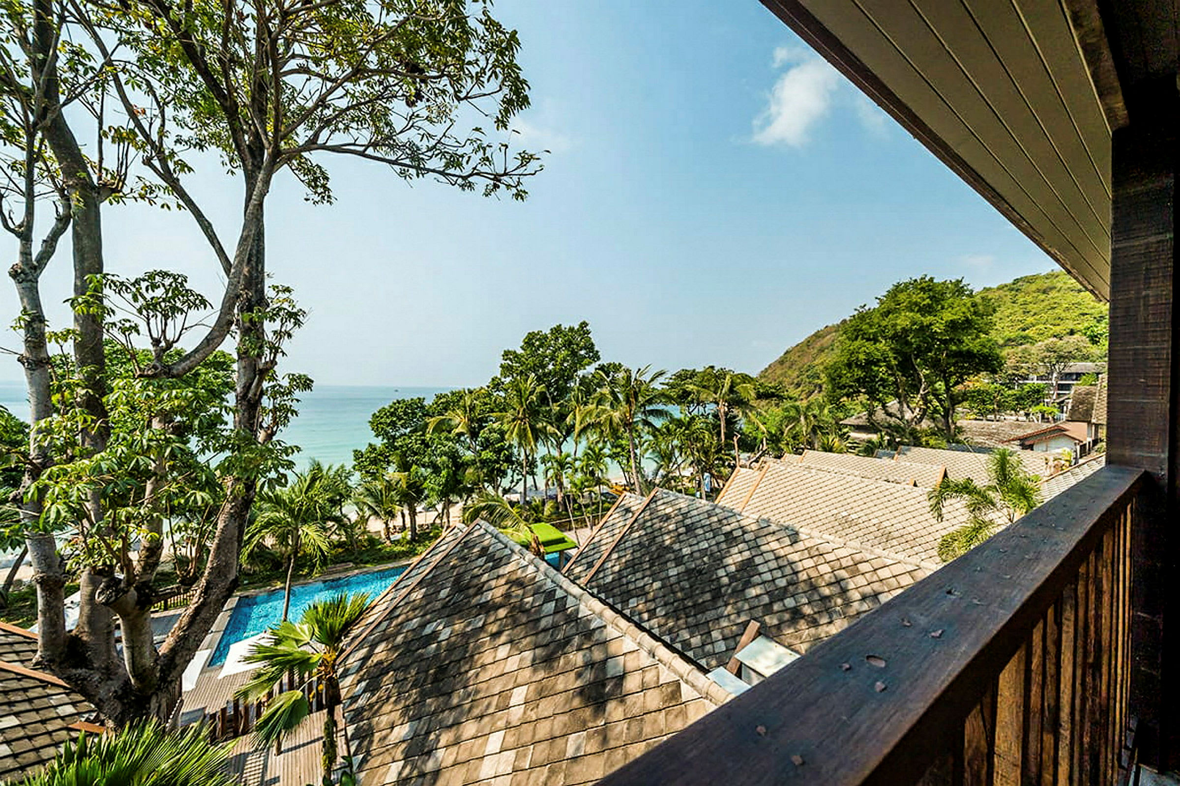 Udsigt over tage, træer og havet med en klar himmel fra en balkon. (AI-genereret tekst)