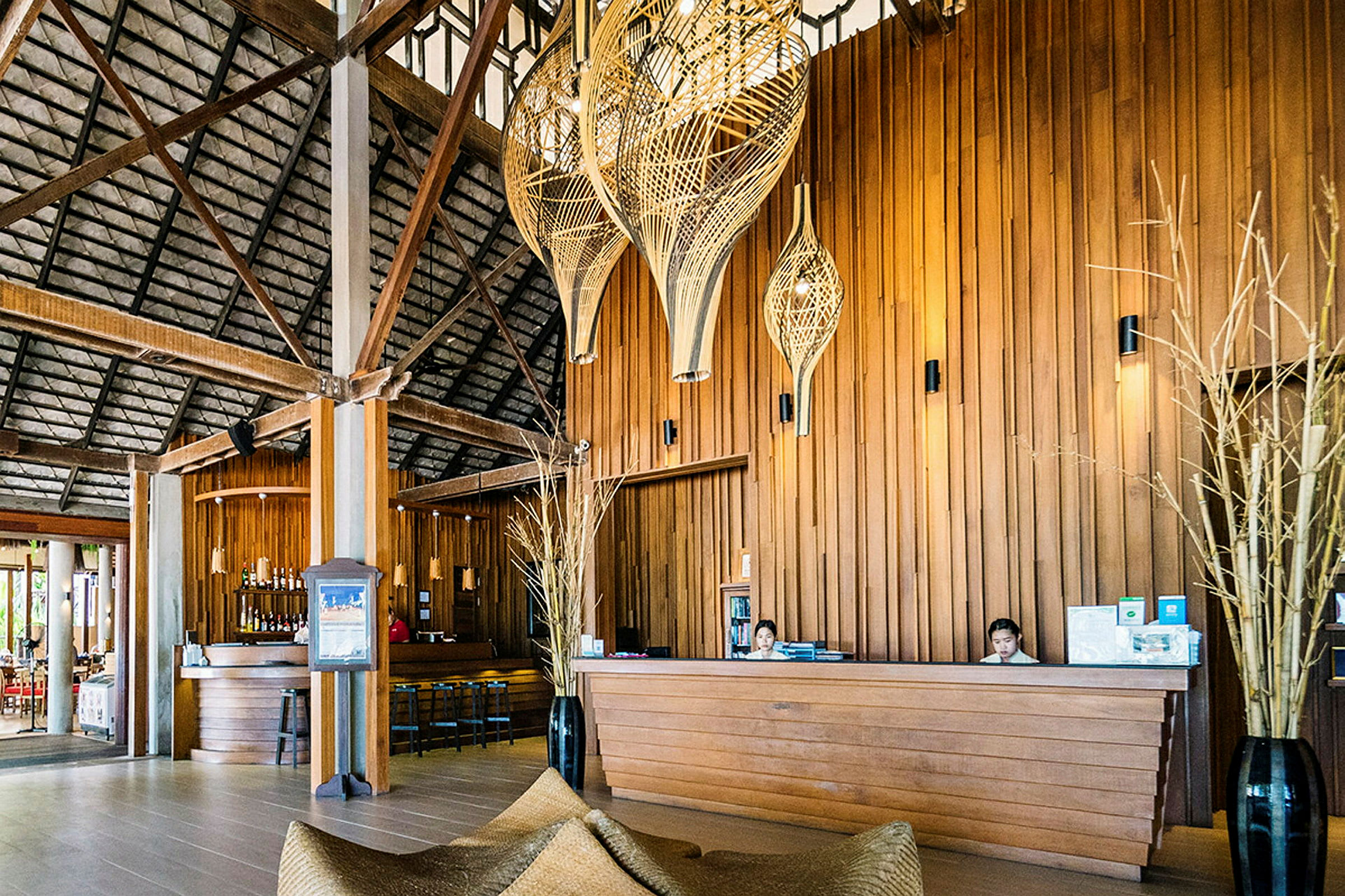 Receptionen på et tropisk resort med træpaneler, lamper og en bar i baggrunden. (AI-genereret tekst)