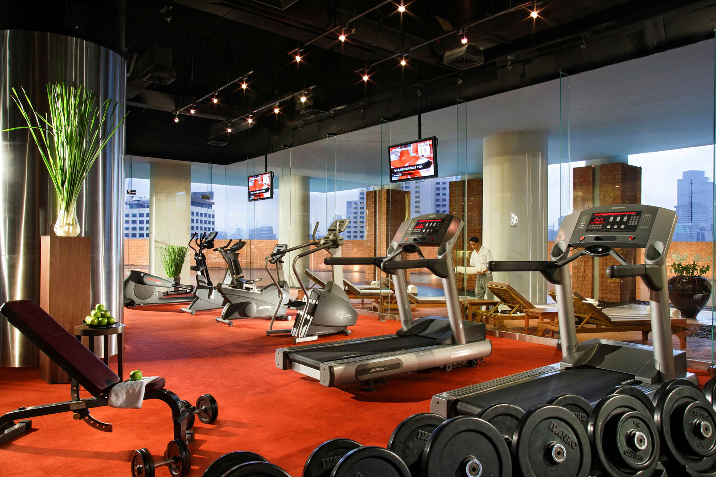 Et fitnesscenter med træningsmaskiner, håndvægte og motionscykler, med store vinduer og udsigt over byens skyline. (AI-genereret tekst)