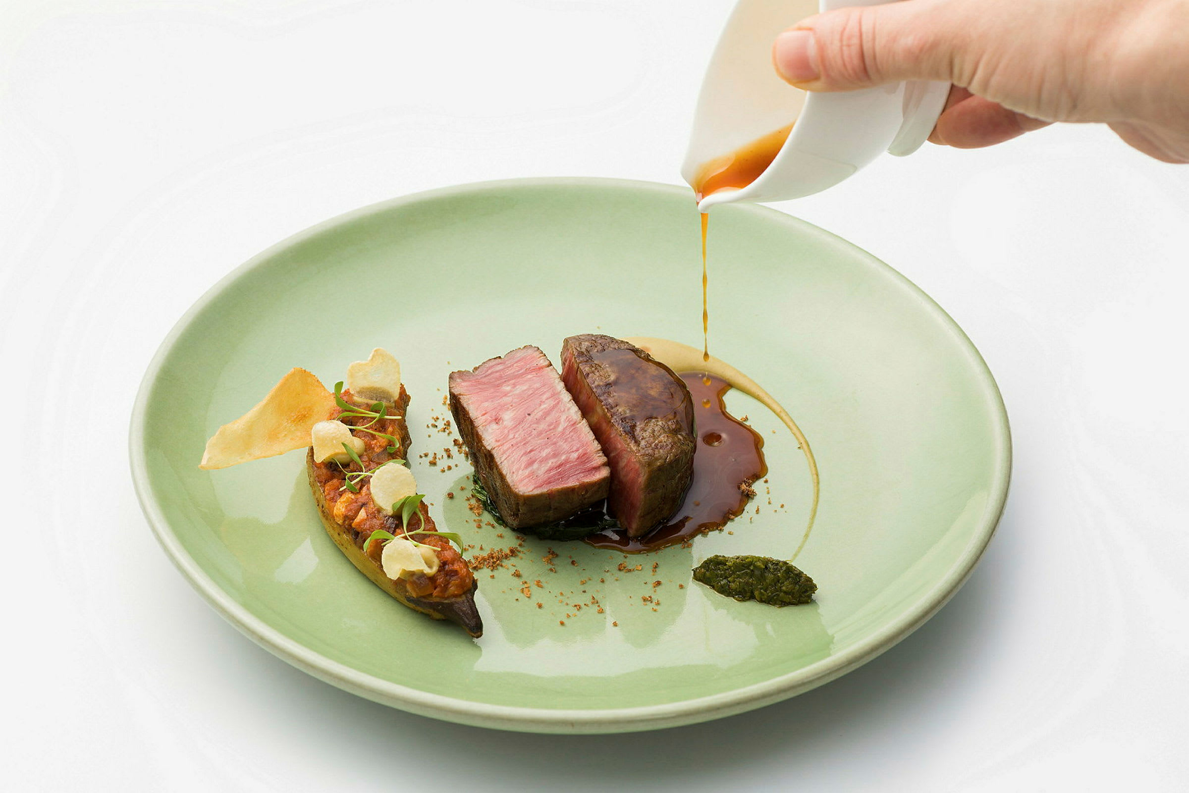 En tallerken med et stykke kød skåret i skiver, hvor der hældes sauce over, sammen med garniture og puré. (AI-genereret tekst)