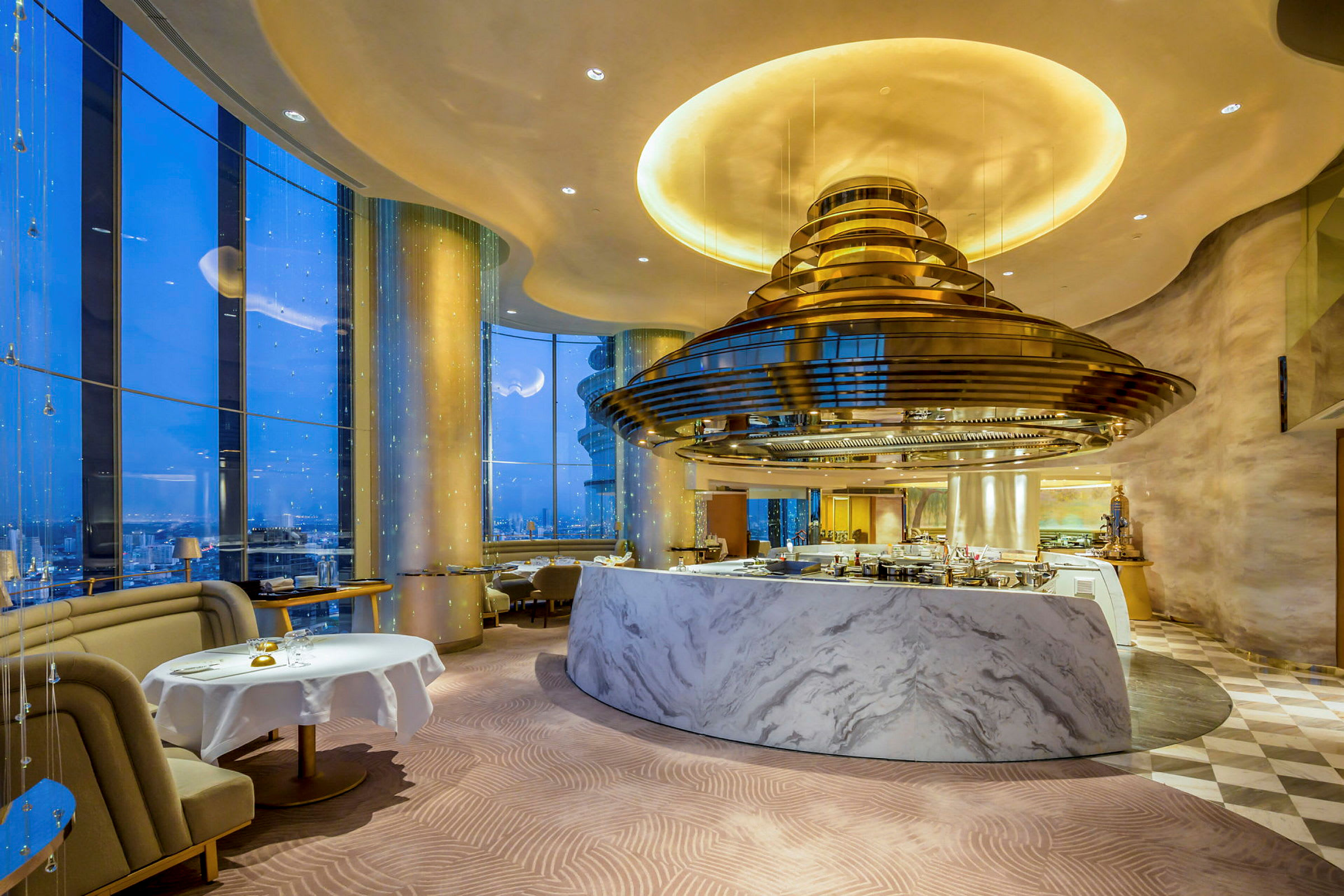 En elegant restaurant med marmorinventar og store vinduer, der giver udsigt over byens natlandskab. (AI-genereret tekst)