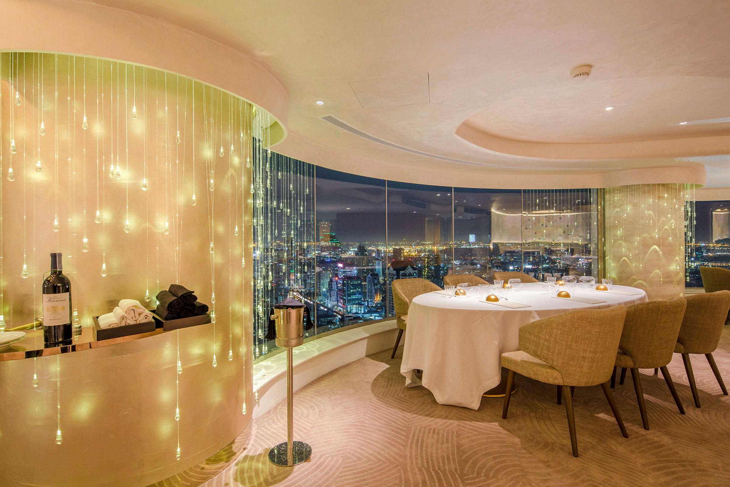 Udsigt over en elegant restaurant med glasvinduer og lysdekorationer, borddekorationer og en flaske vin. (AI-genereret tekst)