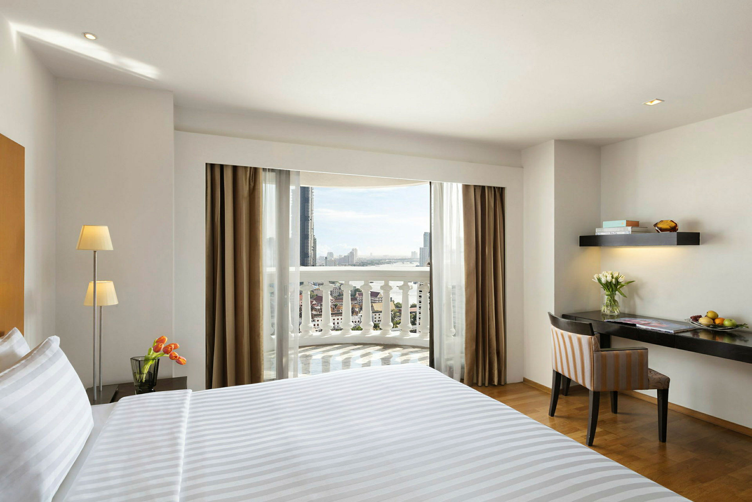 Hotelværelse med en redt seng, et skrivebord og nogle blomster samt en balkon med udsigt. (AI-genereret tekst)