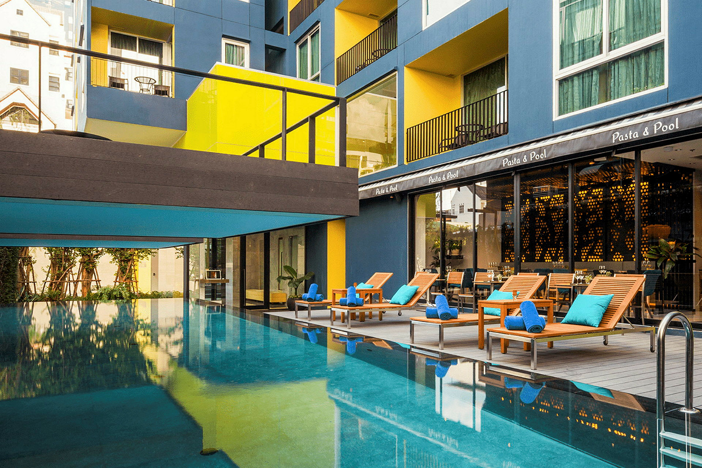 En udendørs pool med liggestole og et moderne hotel i baggrunden. (AI-genereret tekst)