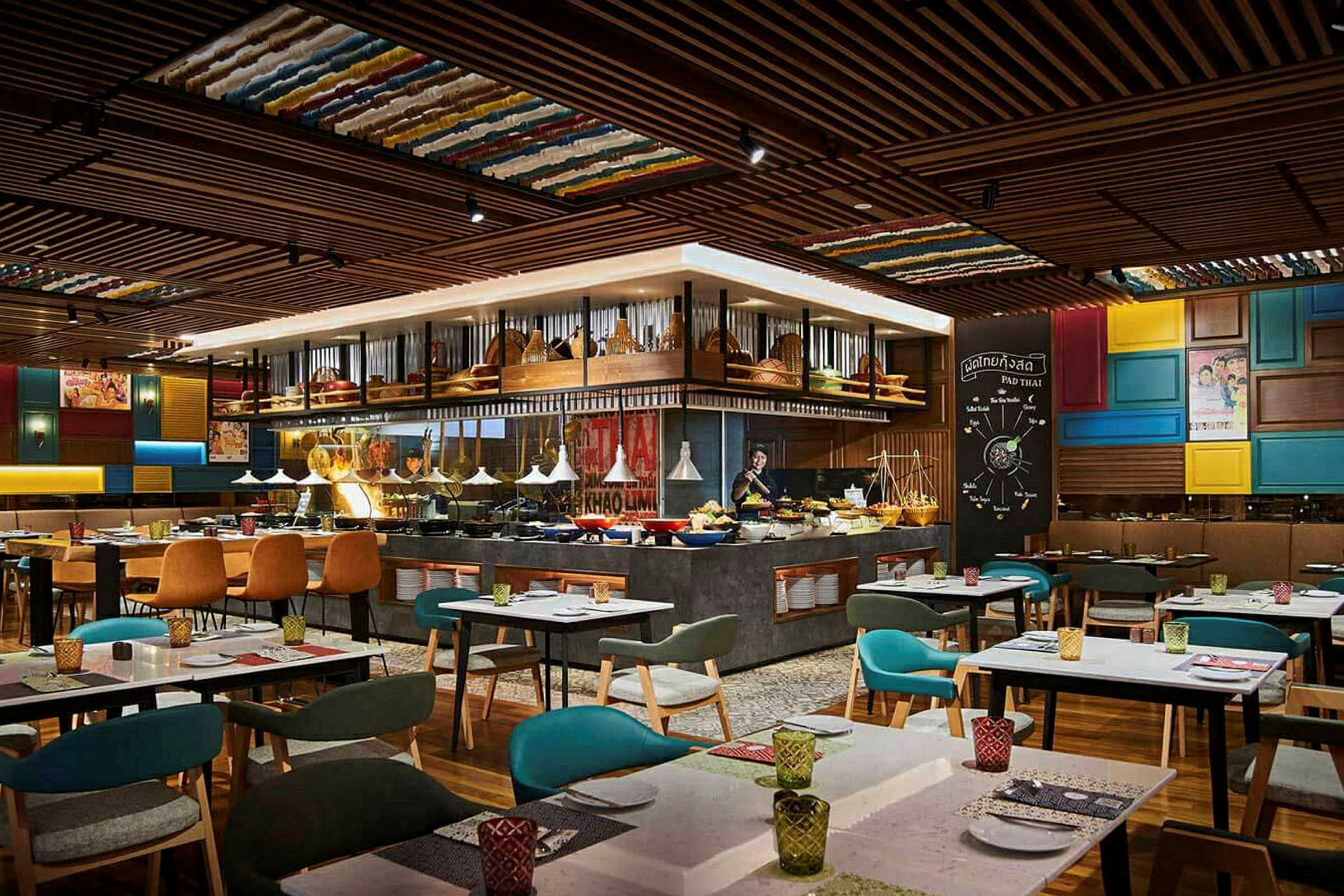 Restaurantinteriør med borde, stole og en madbuffet i midten, omgivet af træt detaljer og farverige dekorative elementer. (AI-genereret tekst)