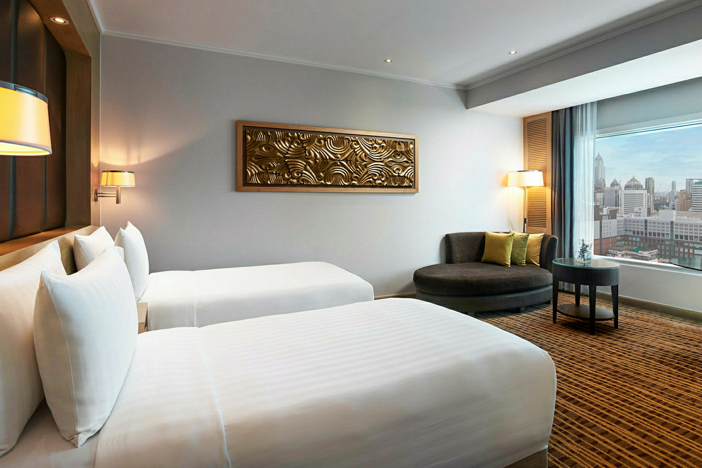 Hotelværelse med to enkeltsenge, dekoration på væggen og siddeområde med udsigt over byen gennem et vindue. (AI-genereret tekst)