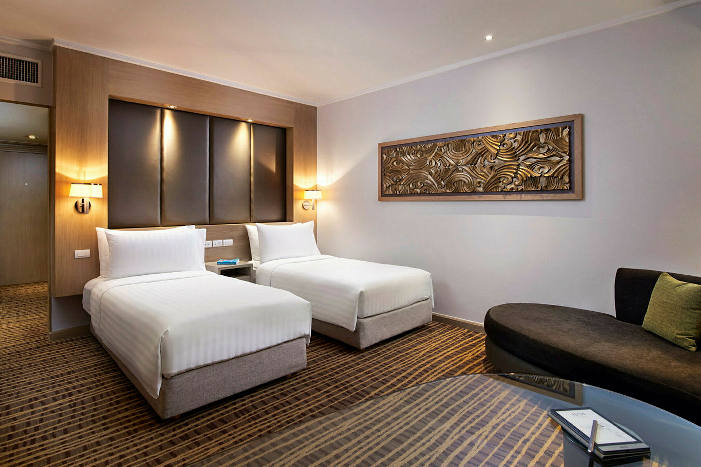 Moderne hotelværelse med to enkeltsenge, en sofa og et bord. (AI-genereret tekst)