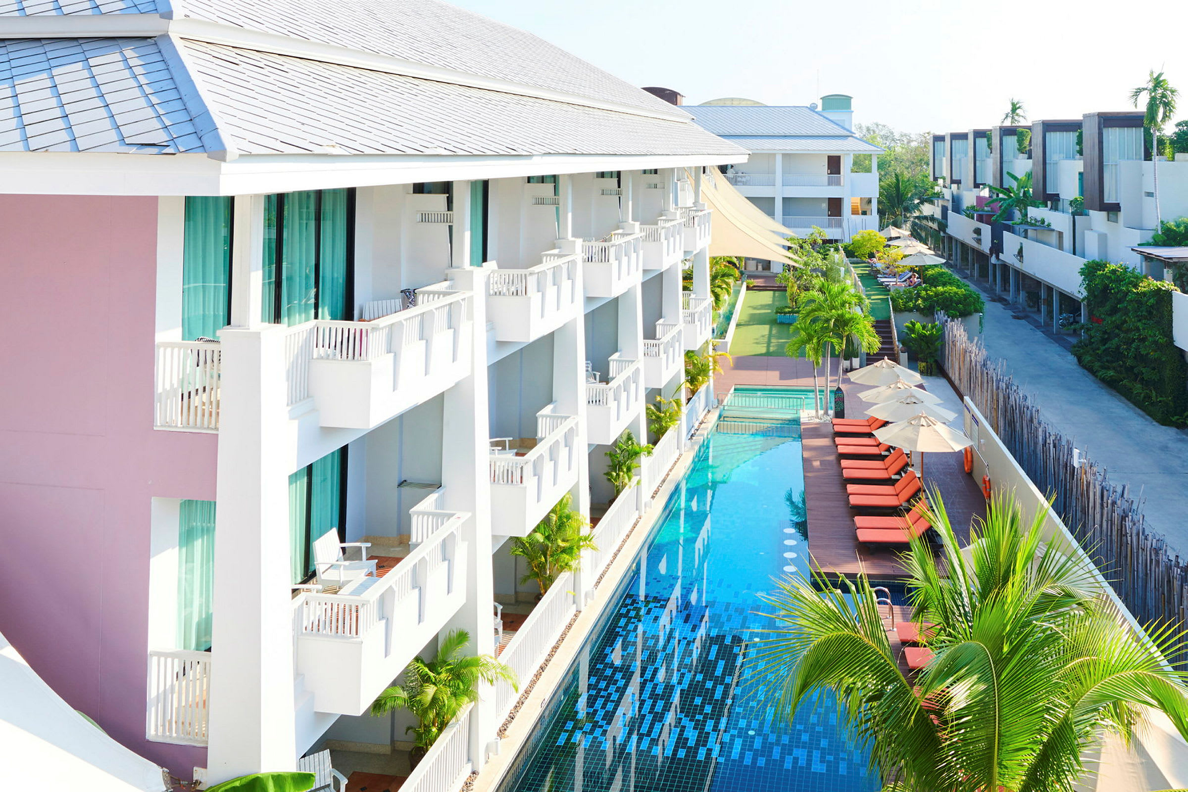 Et hotel med altaner og en lang pool ved siden af solsenge og parasoller. (AI-genereret tekst)