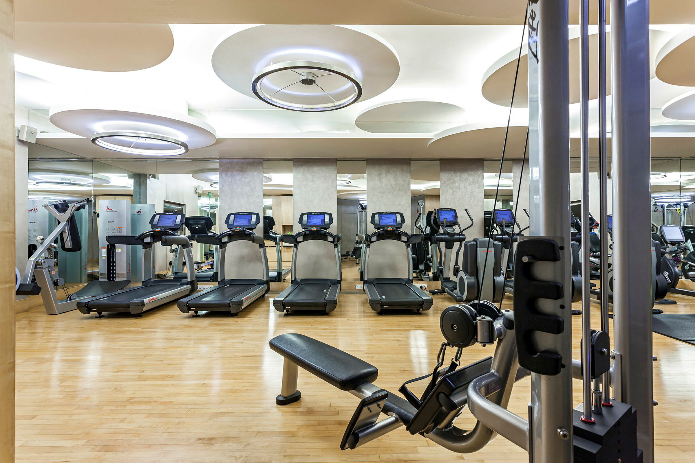 Et fitnesscenter med udstyr som løbebånd og styrketræningsmaskiner. Trægulv og moderne belysning. (AI-genereret tekst)