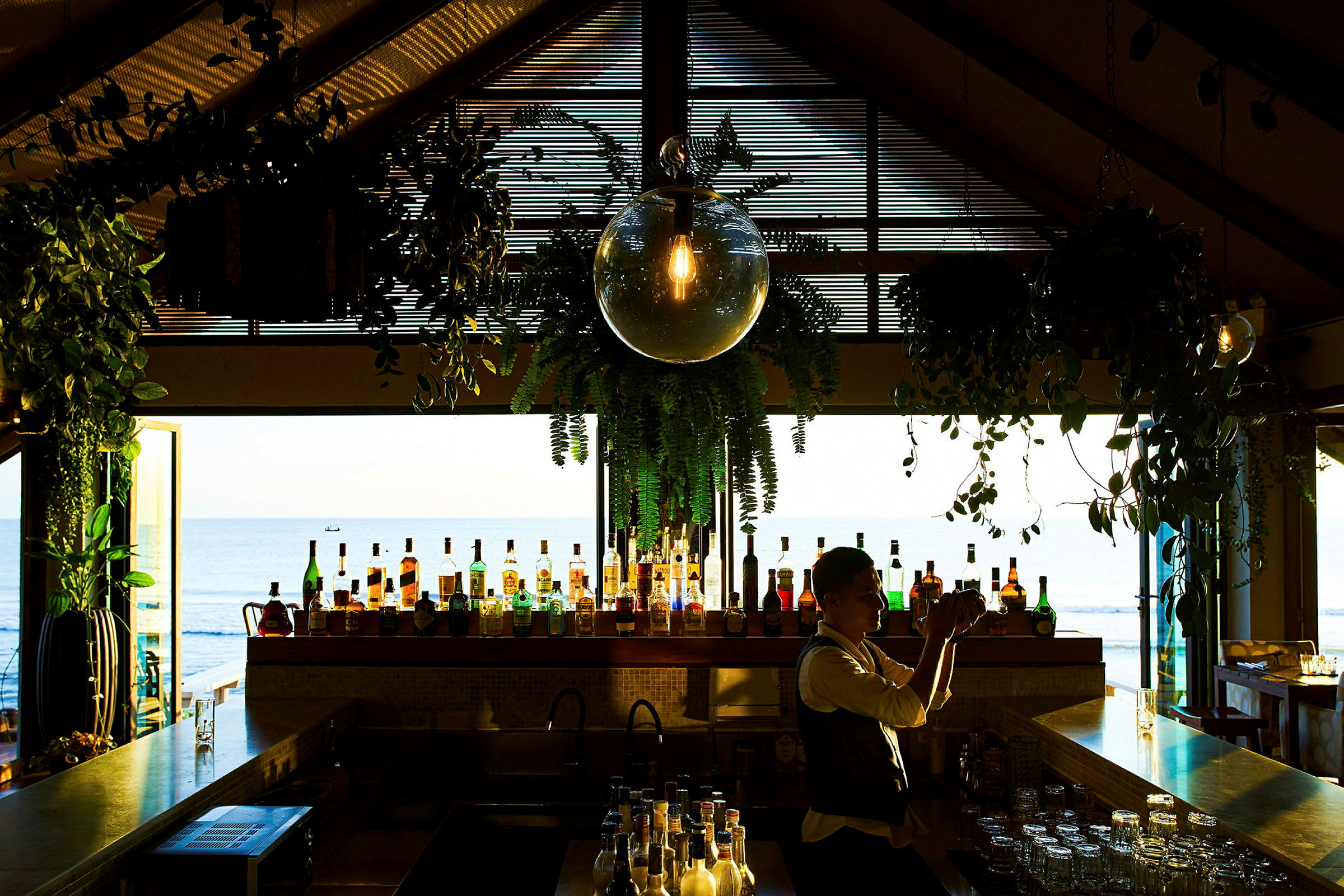 En bar med forskellige flasker og dekorationer i et rum med udsigt over havet. (AI-genereret tekst)
