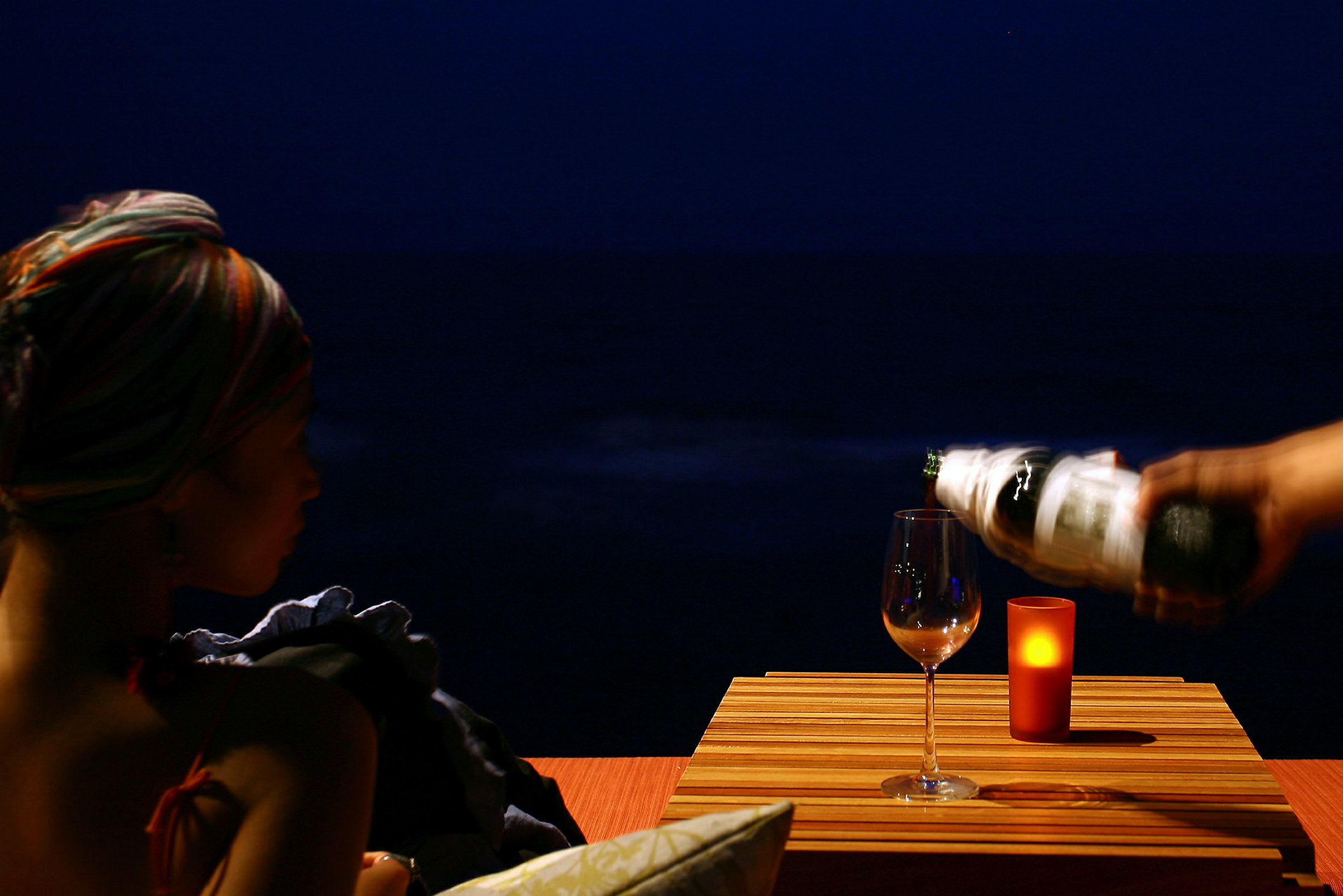 Et glas vin skænkes ved et bord med et lys, mod en mørk baggrund. (AI-genereret tekst)