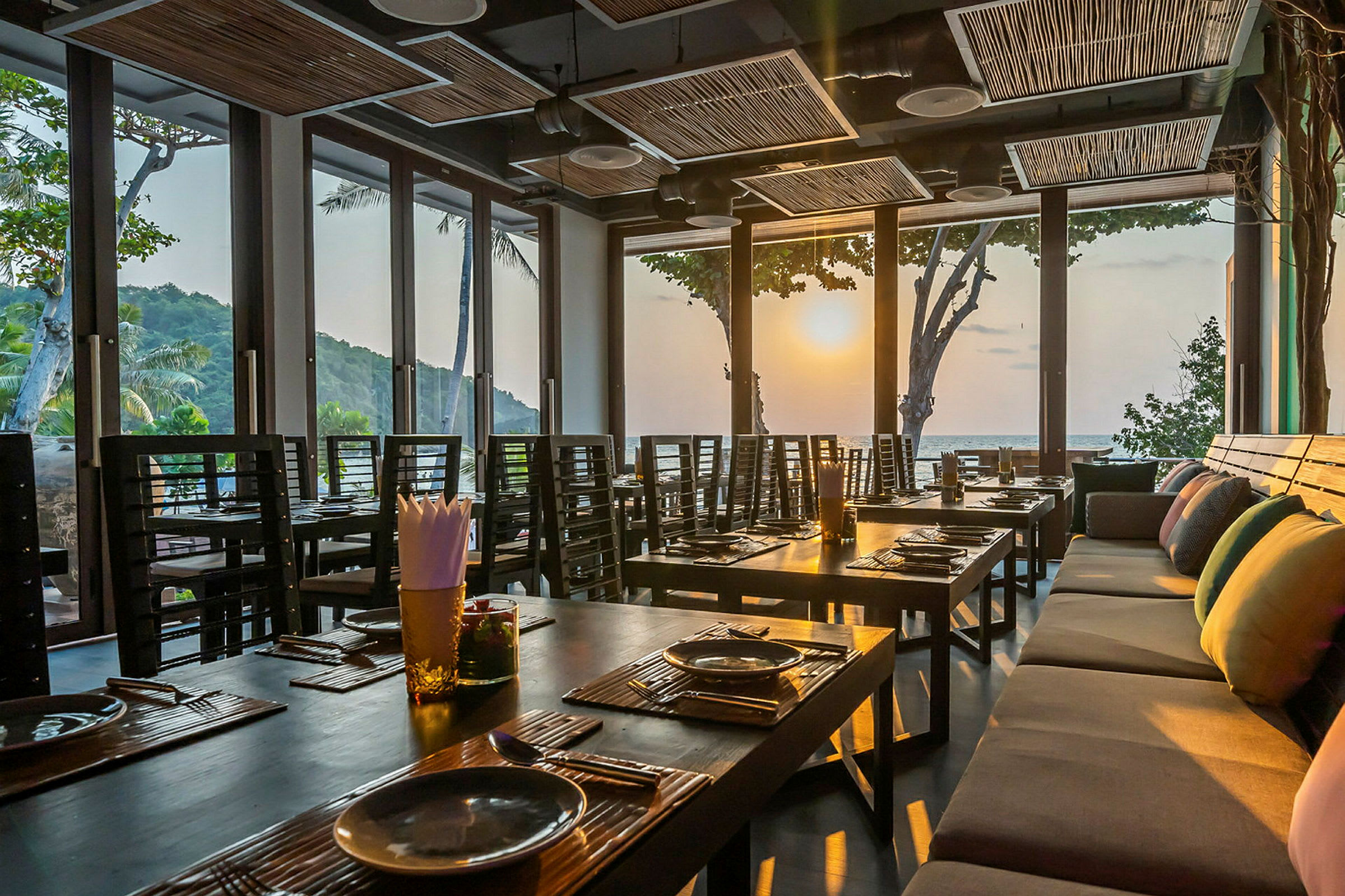 Interiør af en restaurant med dækkede borde og store vinduer, der lukker solnedgangens lys ind. (AI-genereret tekst)