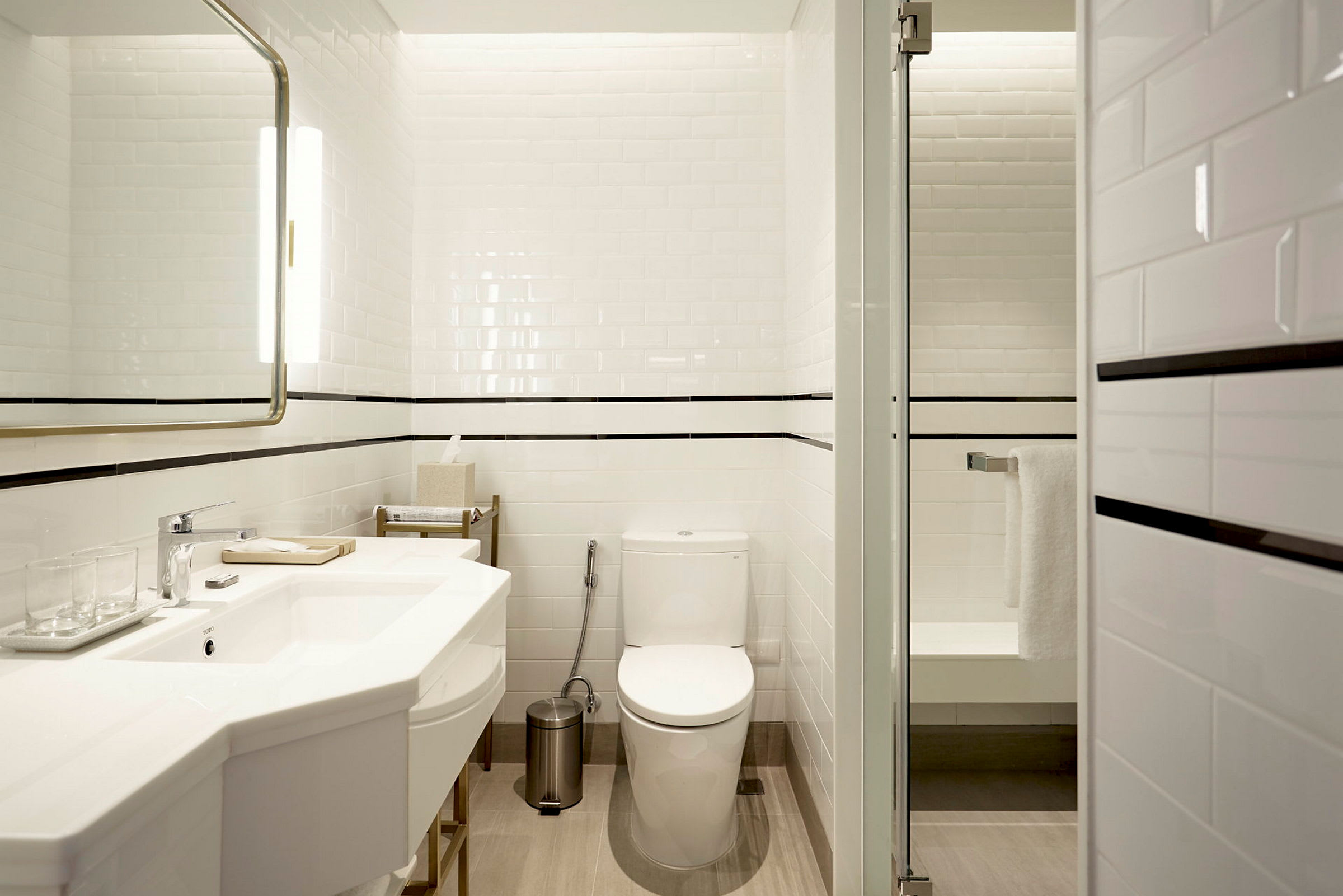Et moderne badeværelse med hvide fliser, et toilet, en håndvask og en brusekabine med glasdør. (AI-genereret tekst)