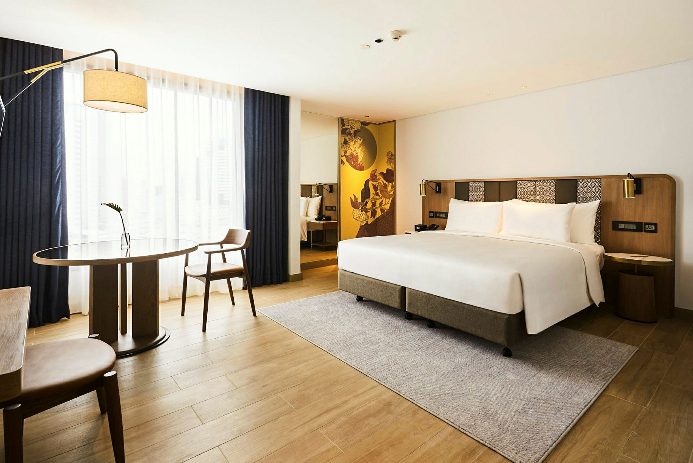 Et moderne hotelværelse med en dobbeltseng, et bord og to stole samt et stort vinduesparti med gardiner. (AI-genereret tekst)