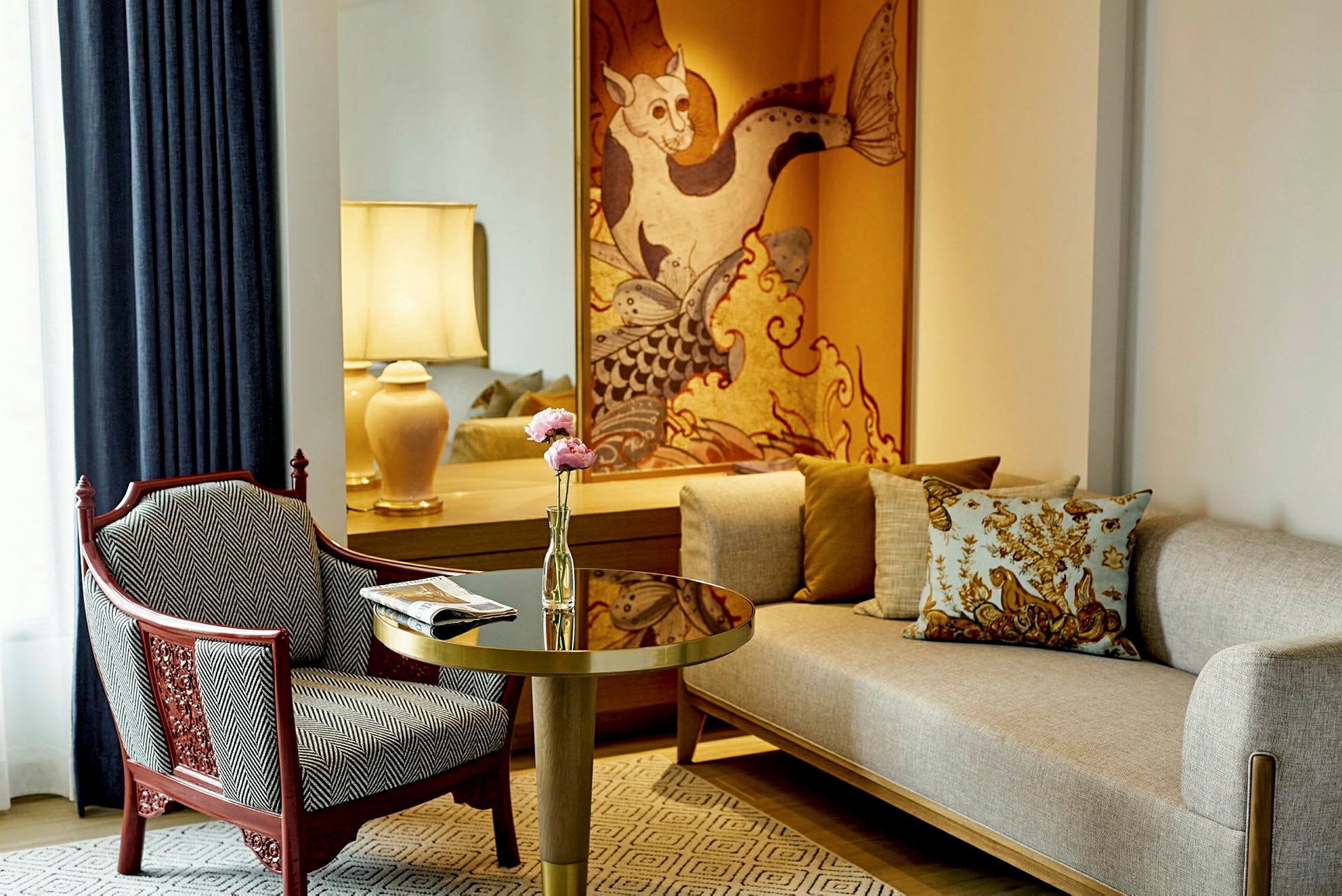 Et elegant rum med en lys sofa, en mønstret lænestol, et bord med blomster og en bordlampe samt dekorativ kunst på væggen. (AI-genereret tekst)