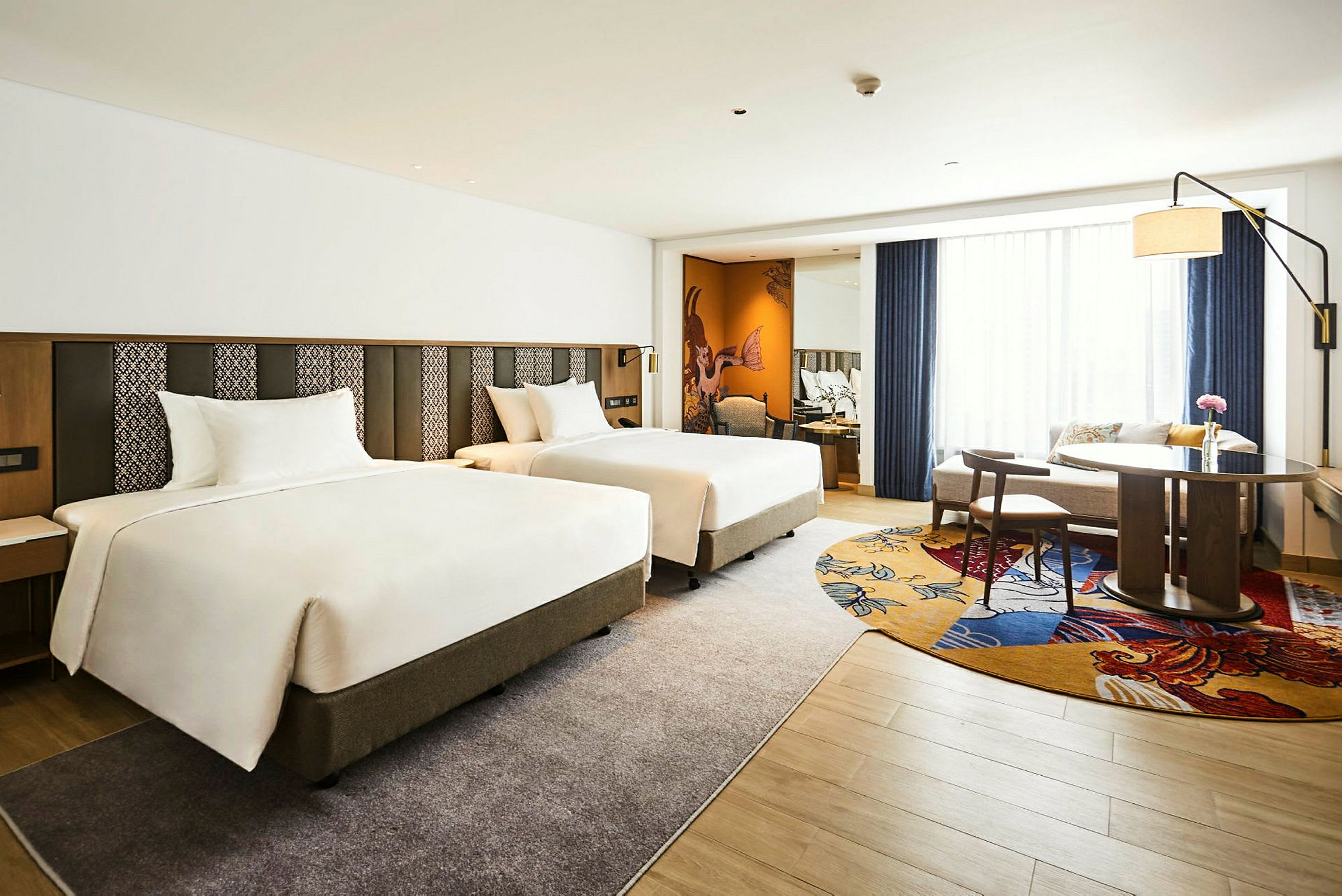 Hotelværelse med to separate senge, et bord med stole samt en sofagruppe. (AI-genereret tekst)