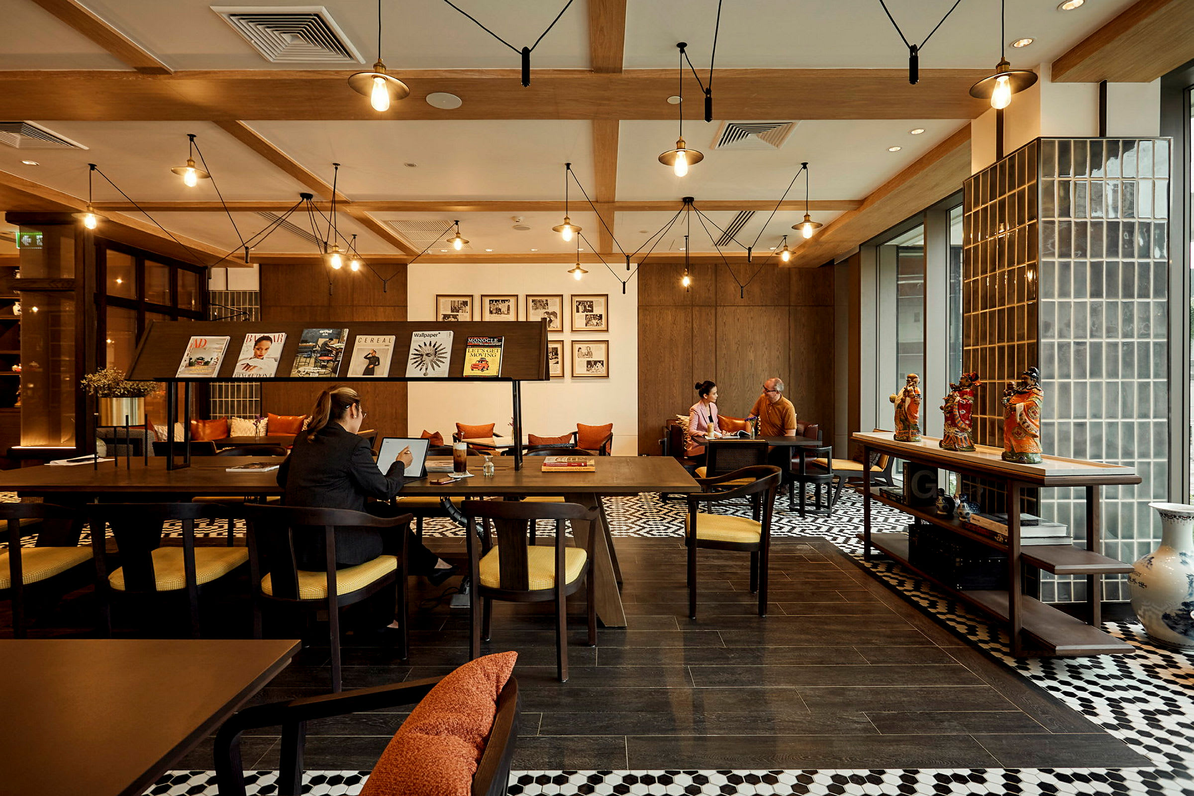 Interiør af en café eller arbejdsområde med træmøbler, dekorationer på bordet og personer, der arbejder eller samtaler. (AI-genereret tekst)