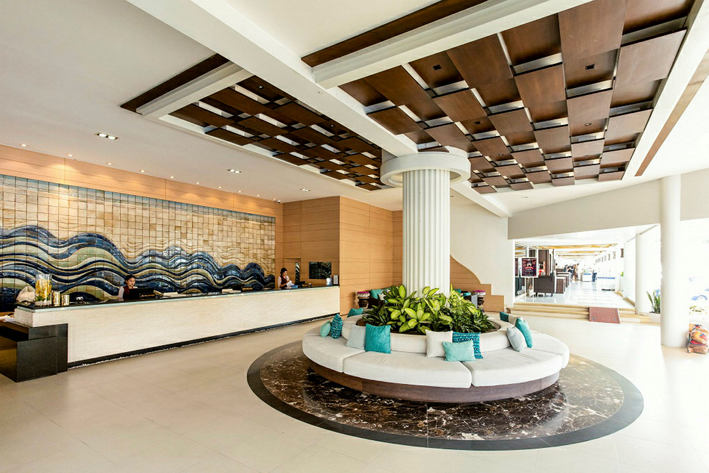 Hotellets lobby med reception, en rund siddegruppe med planter i midten og et dekorativt loftdesign. (AI-genereret tekst)