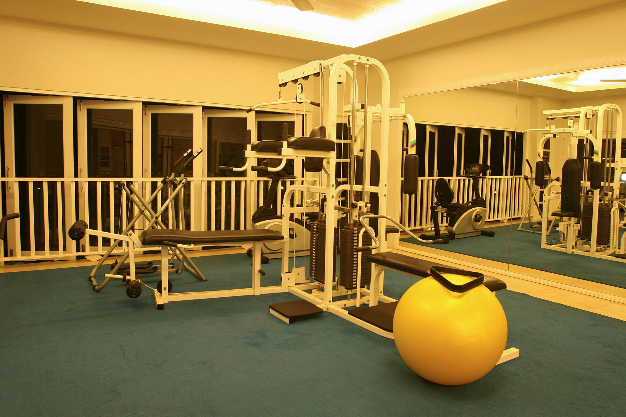 Interiør af et fitnesscenter med træningsudstyr og en gul træningsbold på gulvet. (AI-genereret tekst)
