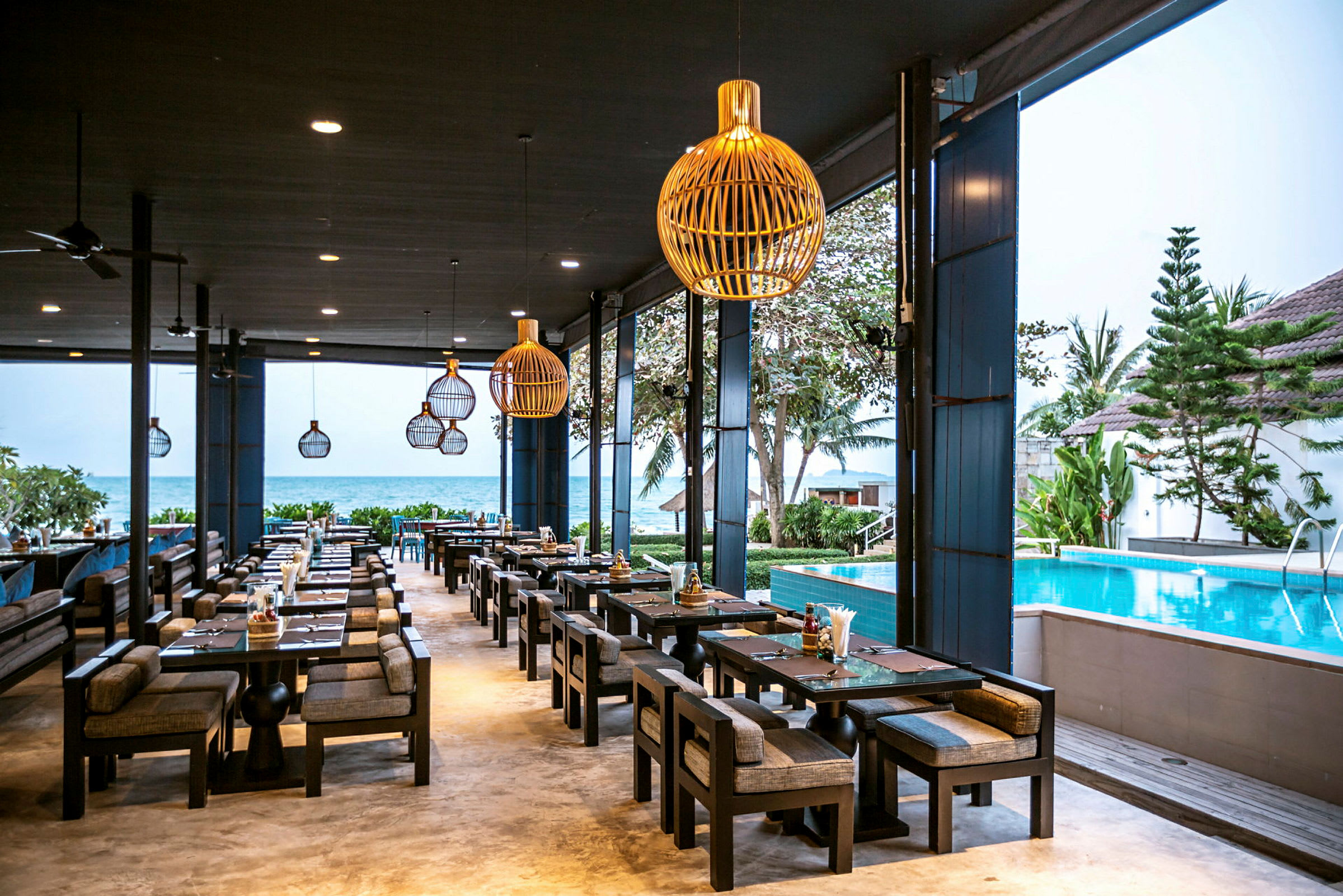 En udendørs restaurant med siddepladser ved en pool, med havet i baggrunden. (AI-genereret tekst)