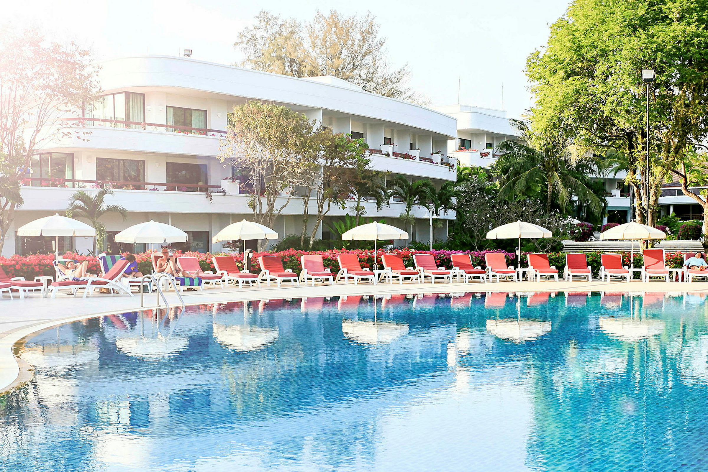 Poolområde med liggestole og parasoller foran et hotel. (AI-genereret tekst)
