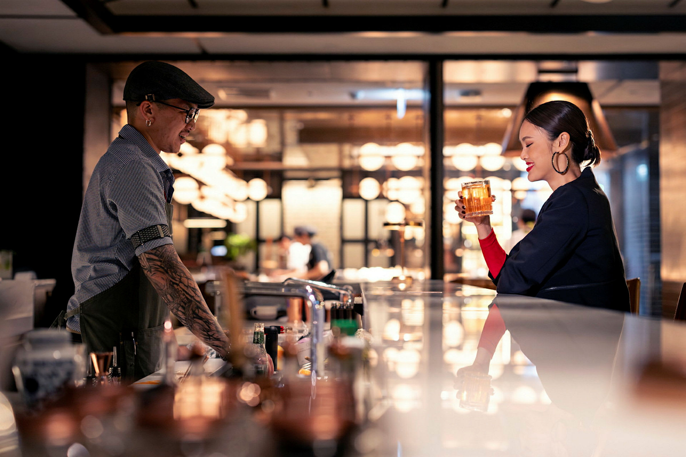 En bar med en bartender iført hat og en gæst, der holder et glas drik. (AI-genereret tekst)