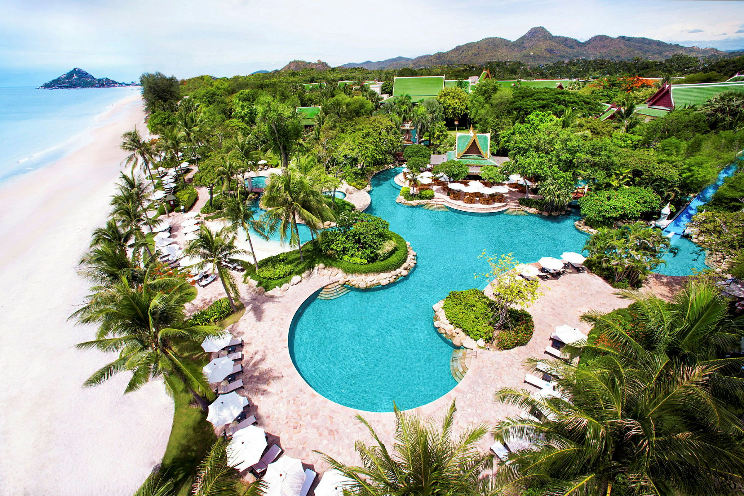En tropisk resort med flere pools, grønne områder og en strand med hvidt sand. (AI-genereret tekst)