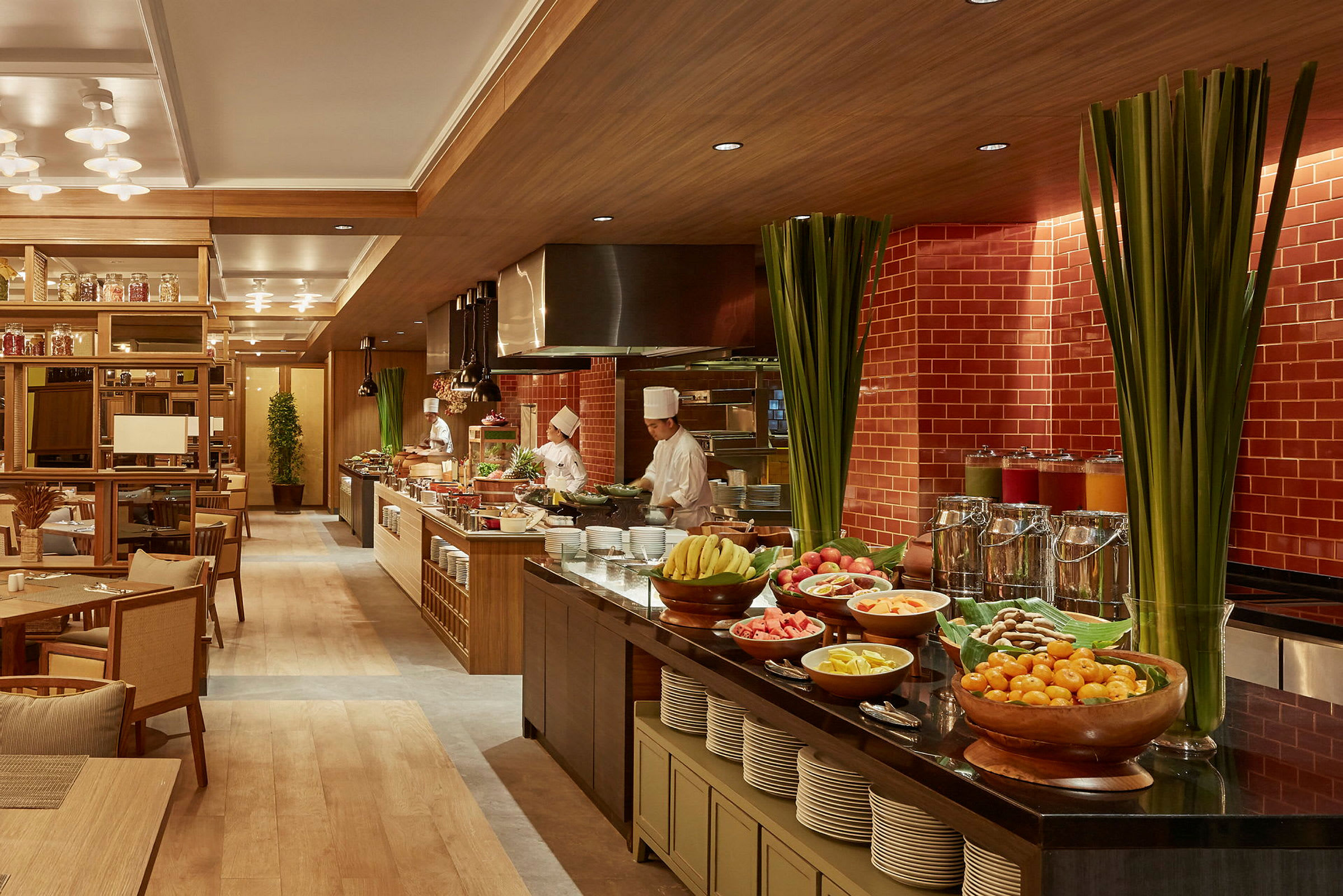 En restaurant med en buffet fremstillet, med forskellige frugter, retter og drikkevarer anrettet. Kokke arbejder bag buffeten. (AI-genereret tekst)
