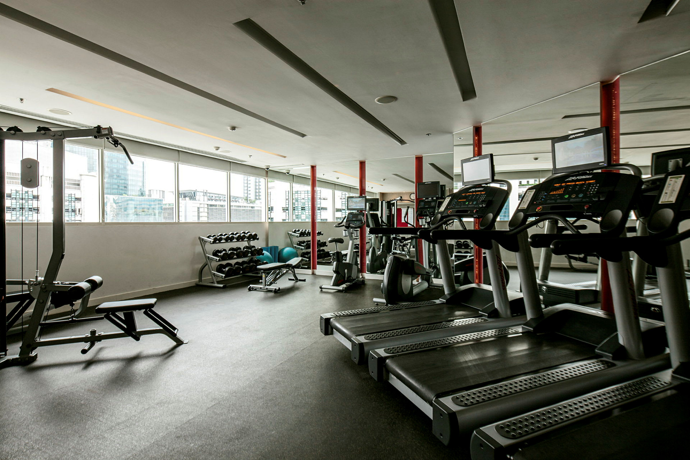 Et fitnesscenter med løbebånd, træningsmaskiner og vægte ved et vindue. (AI-genereret tekst)