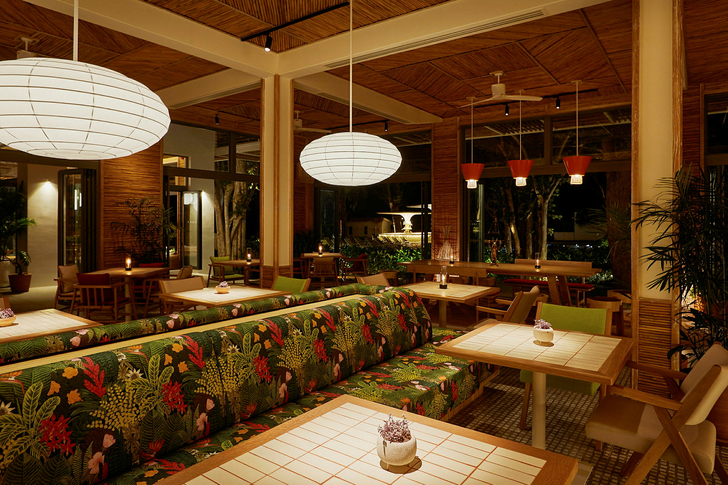 Interiøret i en restaurant med trædetaljer, planter og oplyste borde. Stole og sofaer med farverige mønstre er synlige. (AI-genereret tekst)