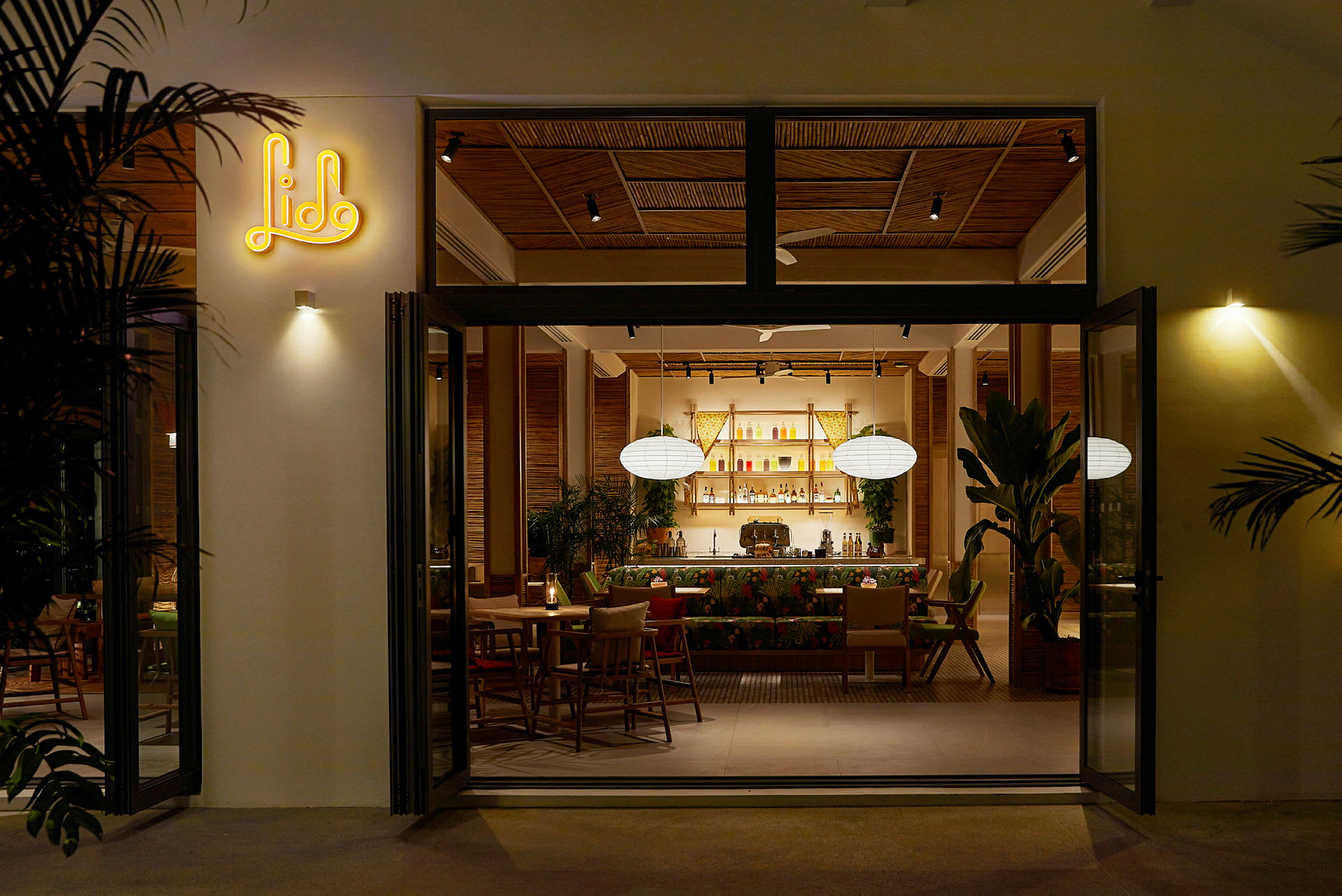 En åben dør til en restaurant med moderne interiør, hvor der er planter og en oplyst bardisk indeni. (AI-genereret tekst)