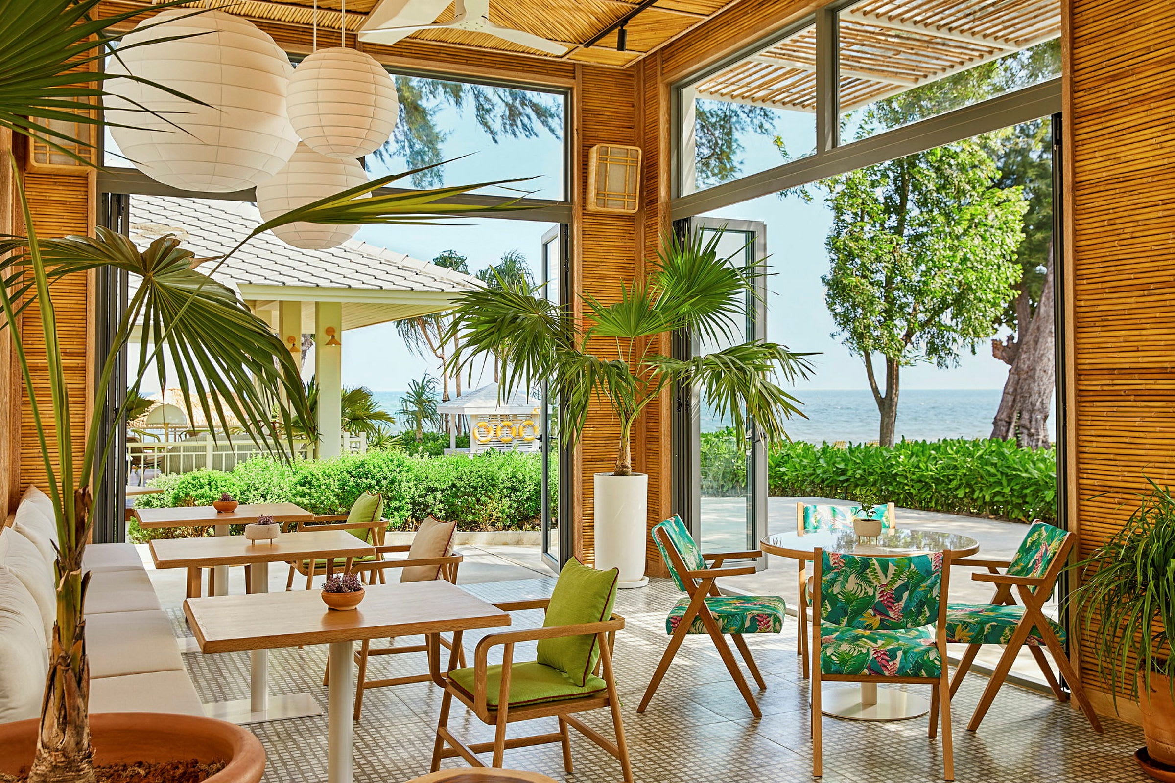 Restaurant med åbne glasvægge, grønne planter og udsigt over havet. (AI-genereret tekst)