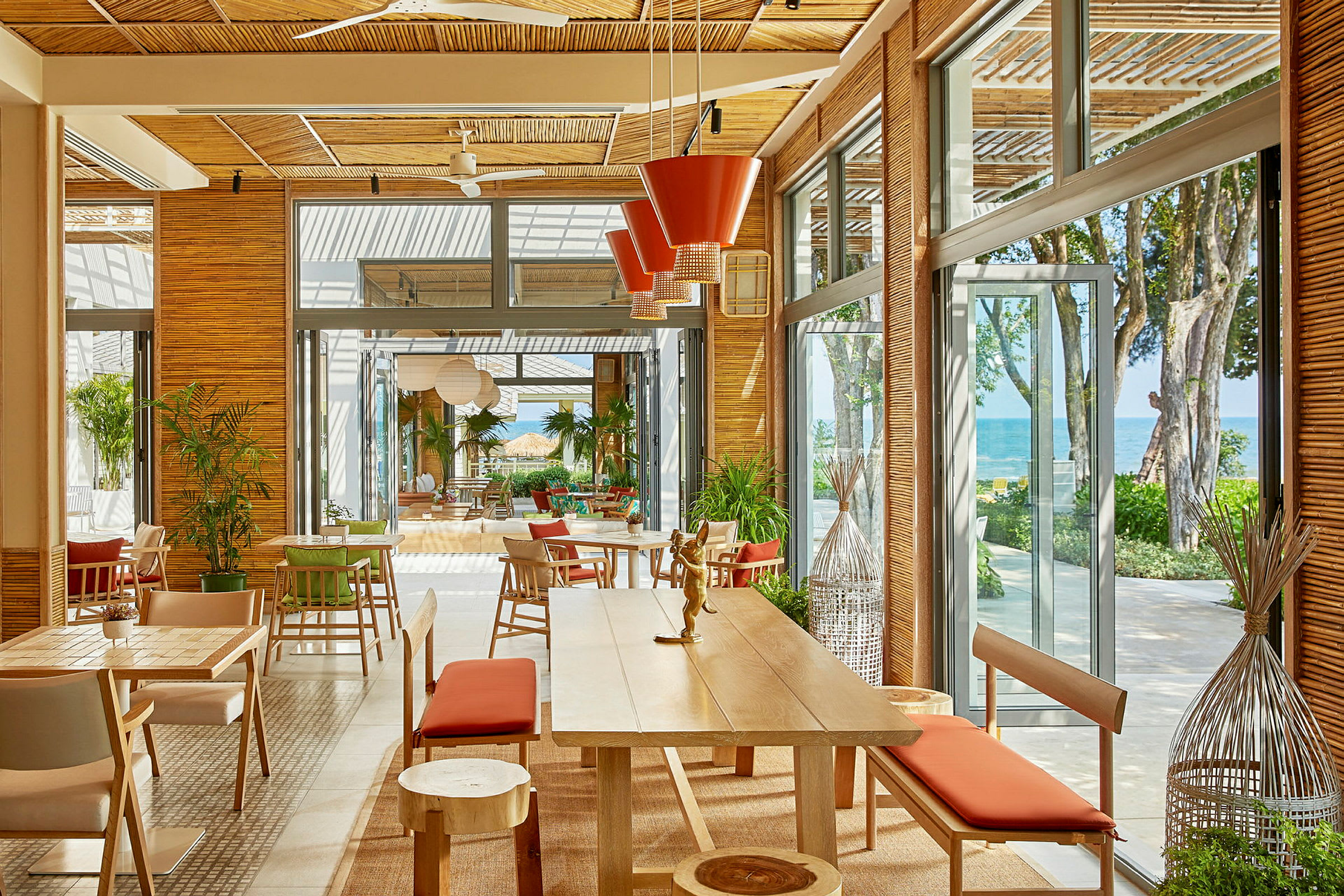 En lys og rummelig restaurant med store vinduer og udsigt til havet. Møblementet er moderne med træmaterialer og røde detaljer. (AI-genereret tekst)
