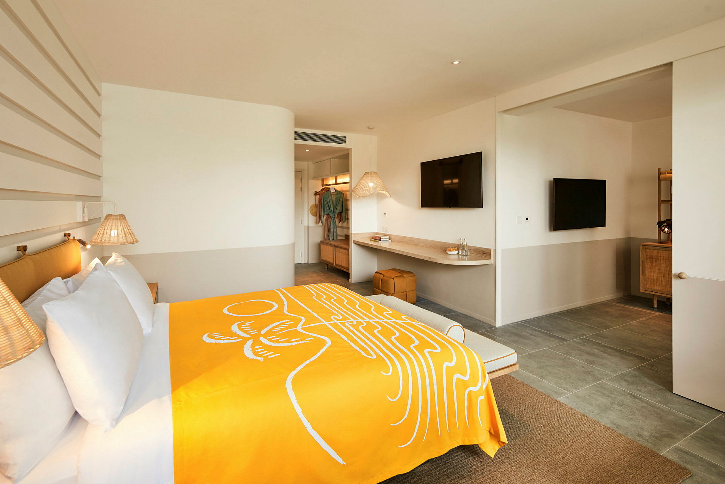 Et moderne hotelværelse med en bred seng dækket med et gult tæppe, vægmonterede lamper og en skrivebordsoverflade med et TV ovenover. (AI-genereret tekst)