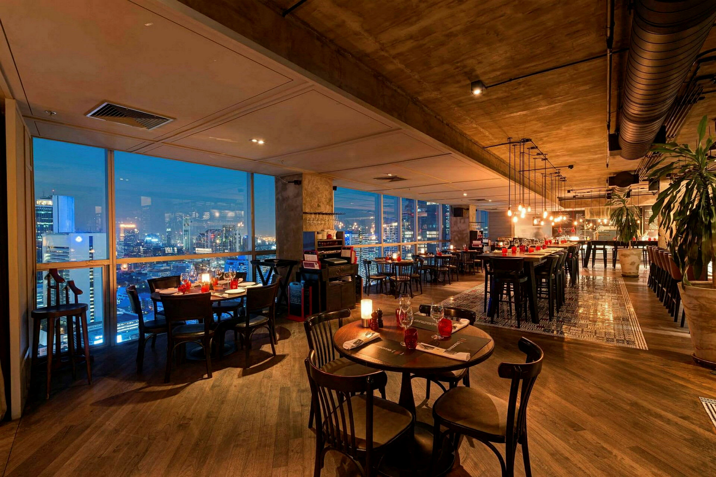En elegant restaurant med moderne møbler, vinduer der viser en byudsigt om aftenen og belysning, der skaber en hyggelig atmosfære. (AI-genereret tekst)