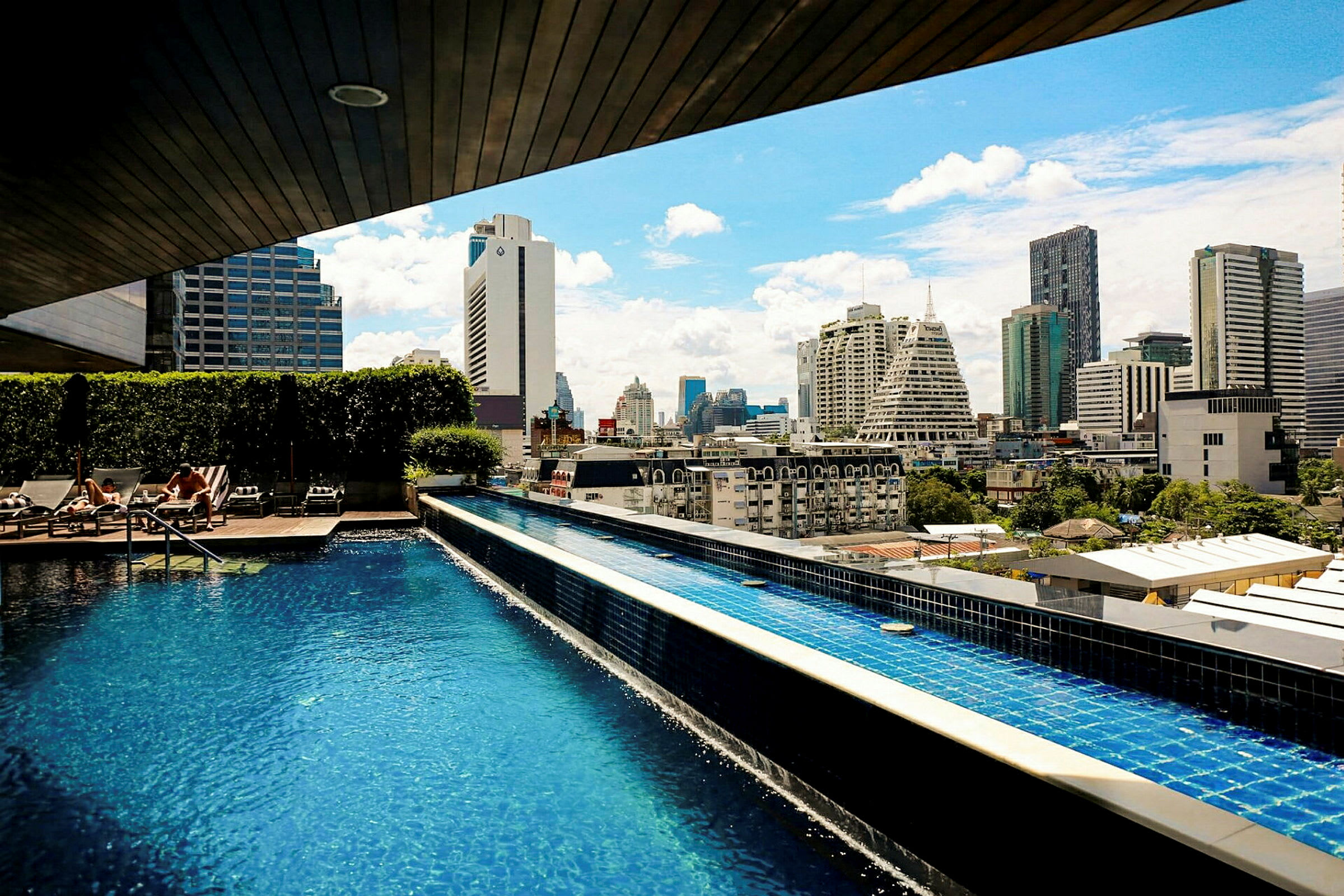 En pool på en tagterrasse med udsigt over byens skyline under en solrig himmel. (AI-genereret tekst)