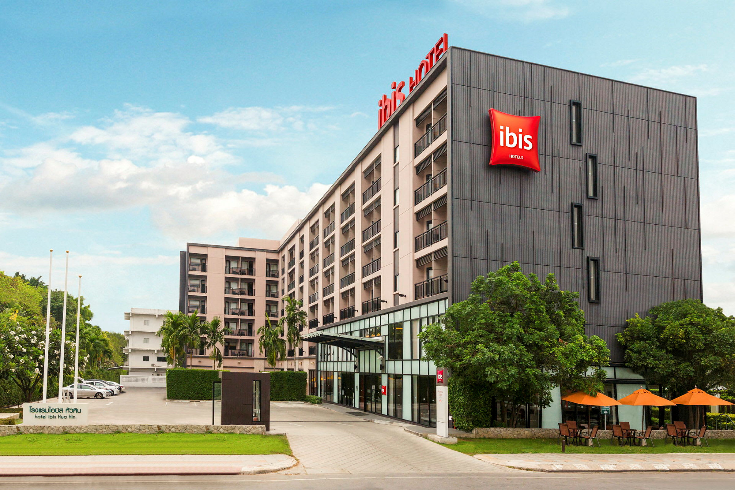 Billede af facaden på et fler-etagers hotel med hotelskilt og omgivende beplantning. (AI-genereret tekst)