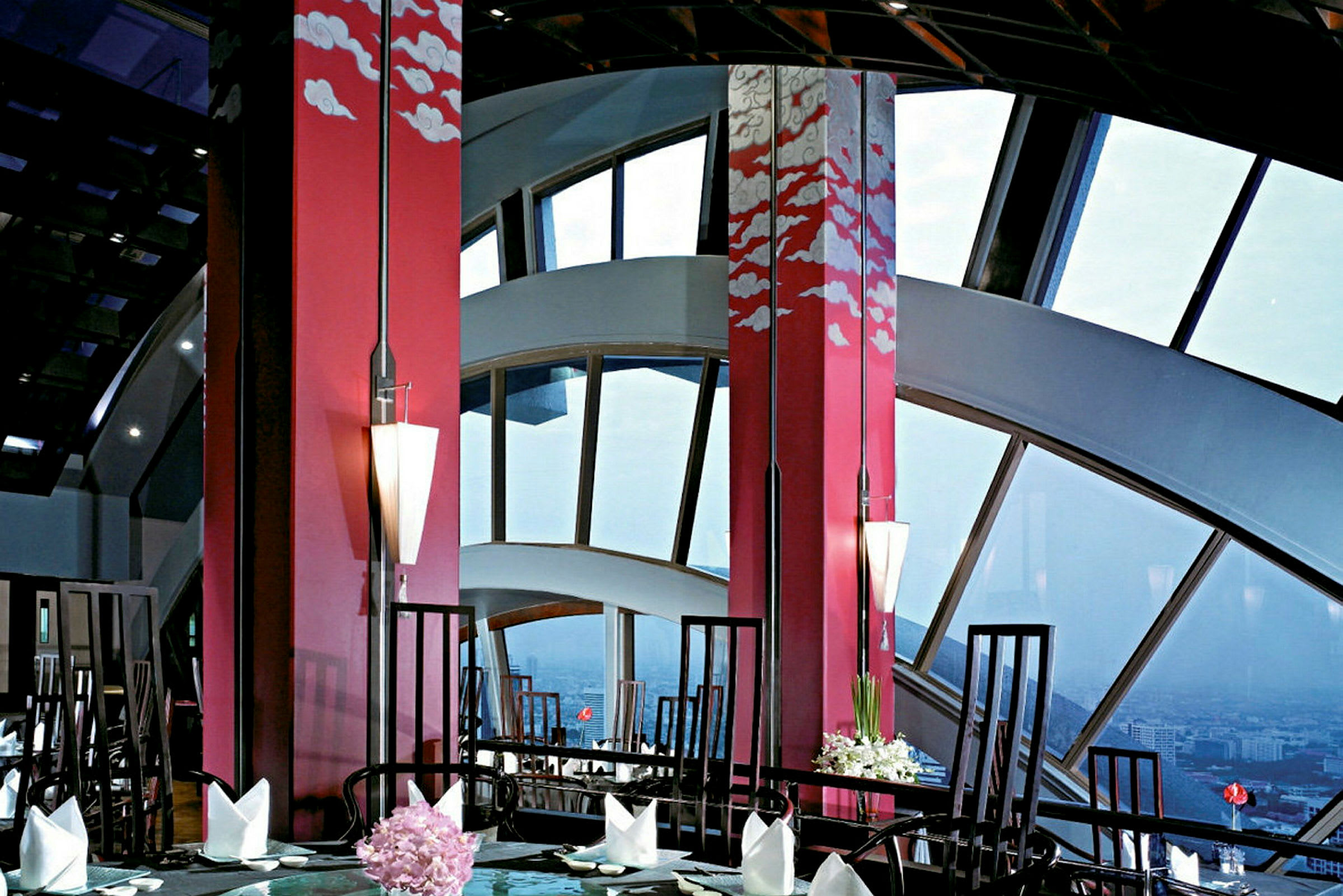En elegant restaurant med store vinduer og rød indretning udsmykket med kunstneriske skymotiver. (AI-genereret tekst)