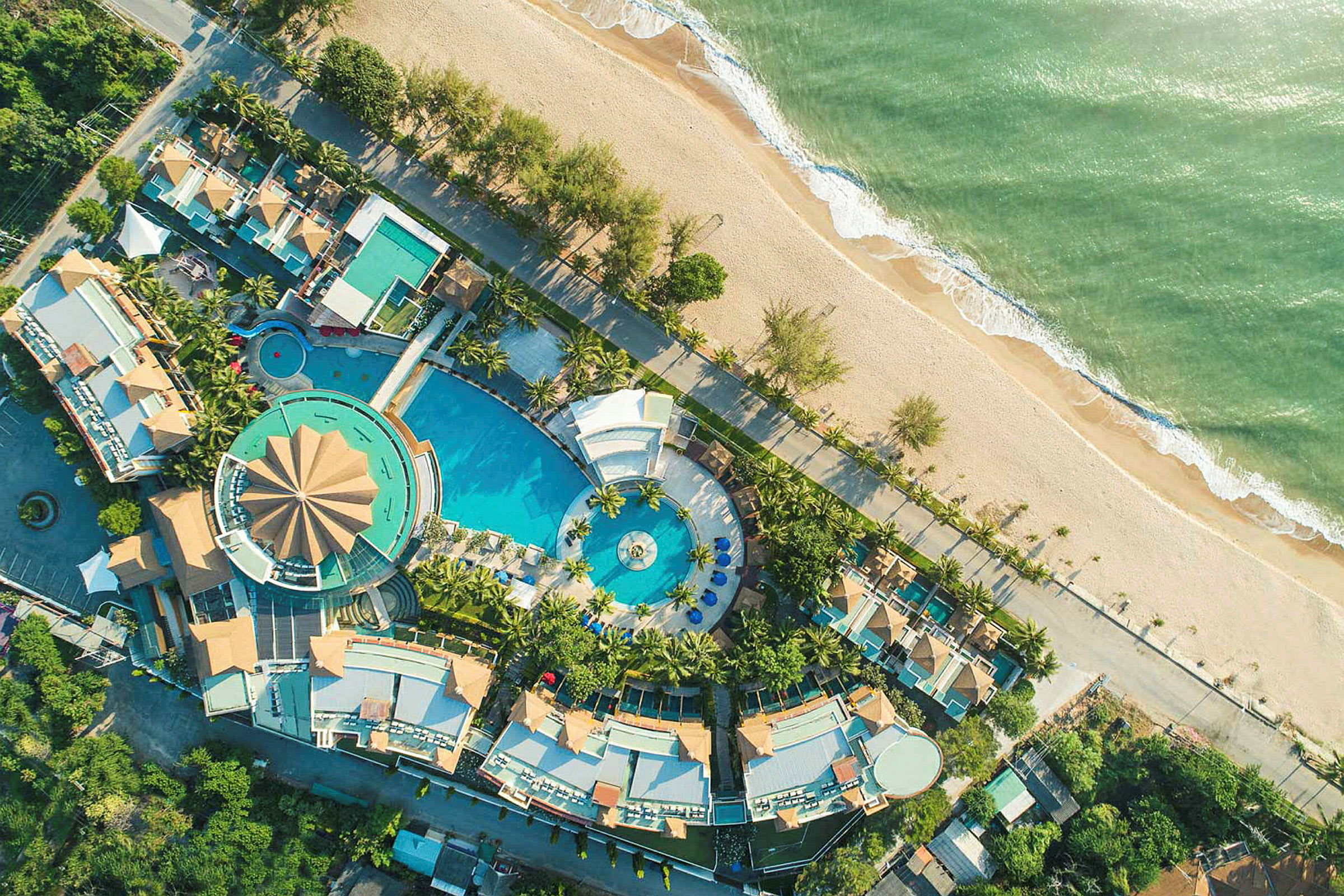 Luftfoto af en resort med poolområde og omkringliggende bygninger ved stranden. (AI-genereret tekst)