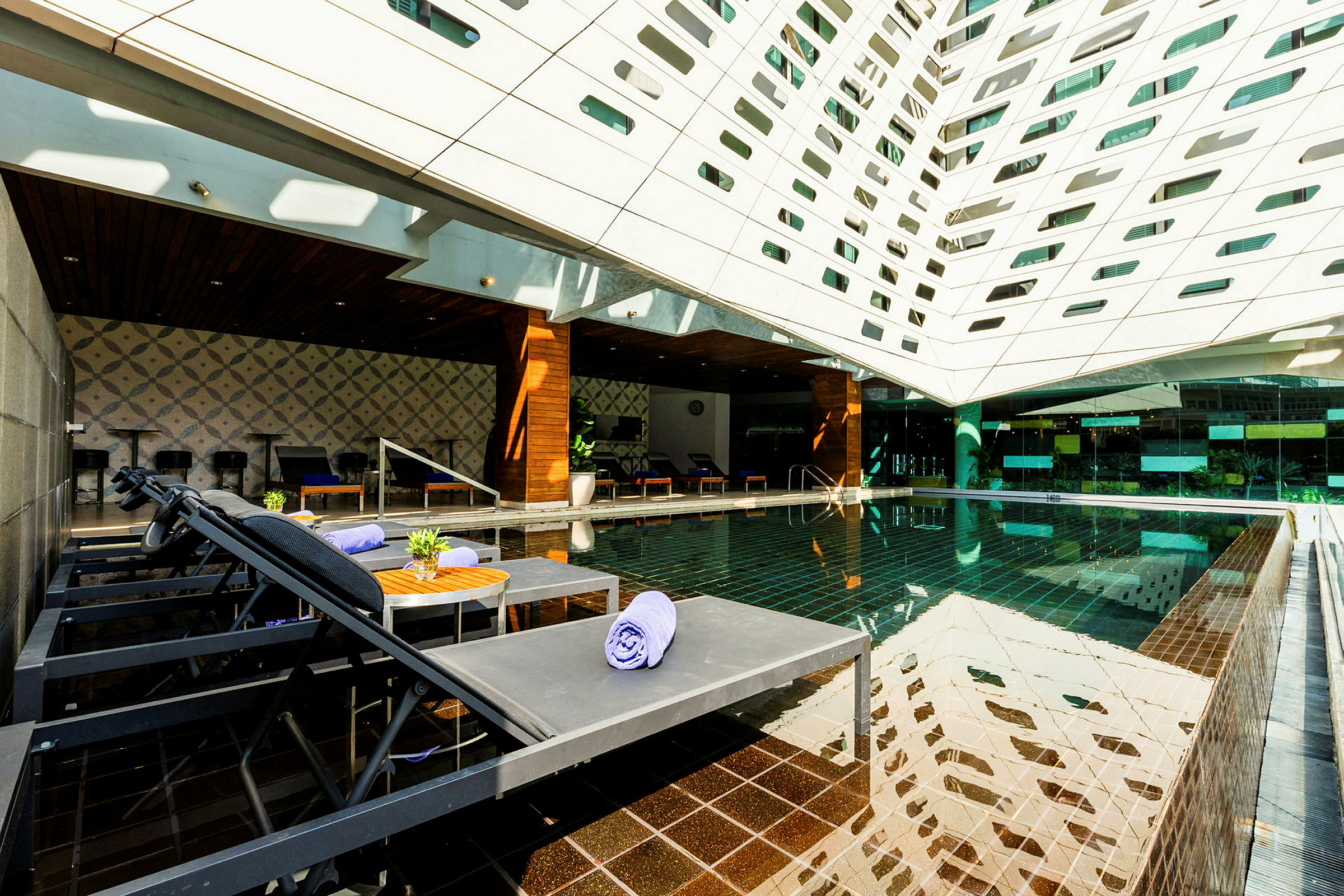 Et moderne udendørsområde med en pool, liggestole og et tag dækket af geometriske åbninger. (AI-genereret tekst)