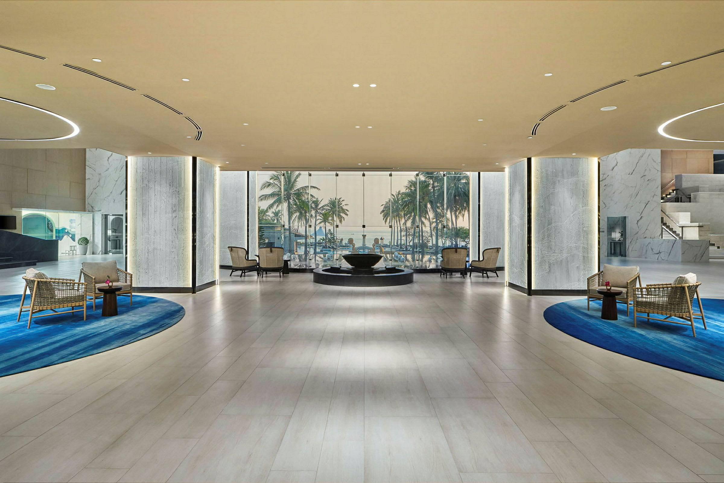 Moderne hotellobby med siddeområder, designede tæpper og en baggrundsudsigt over palmer og himmel gennem store glaspartier. (AI-genereret tekst)